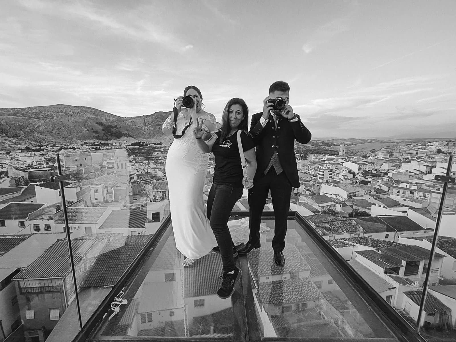 eme entre los dos novios, los tres con sus cámaras, sobre el mirador de cristal de un pueblo blanco