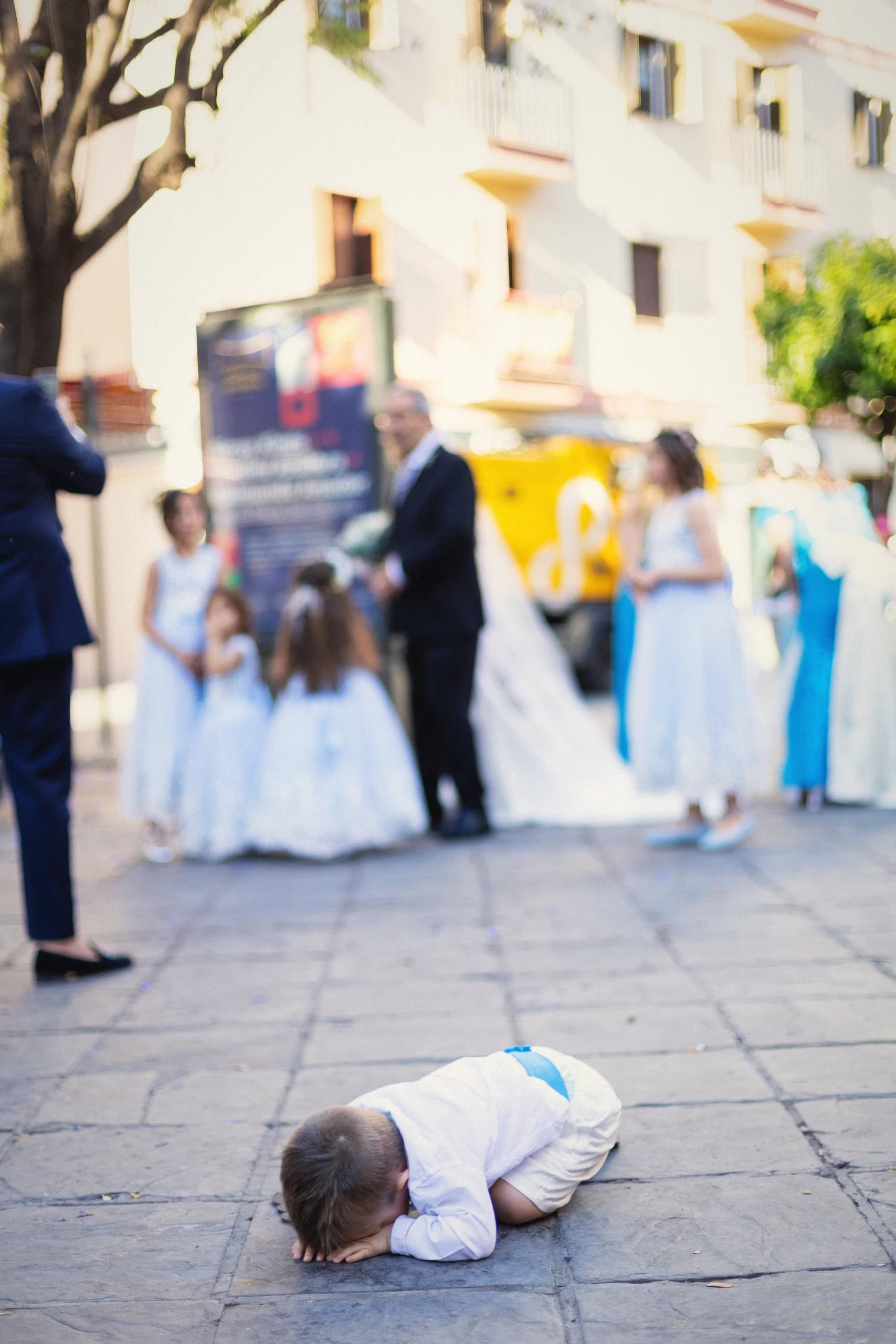 Un niño tirado en el suelo de la calle mientras los novios y los invitados salen de la iglesia detrás