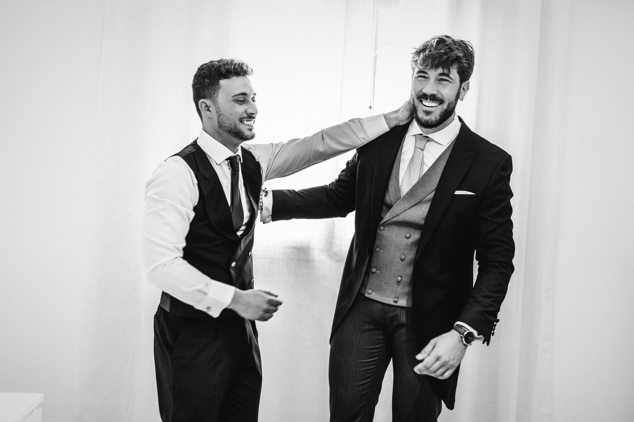 El novio y un amigo riéndose mientras se visten, en blanco y negro
