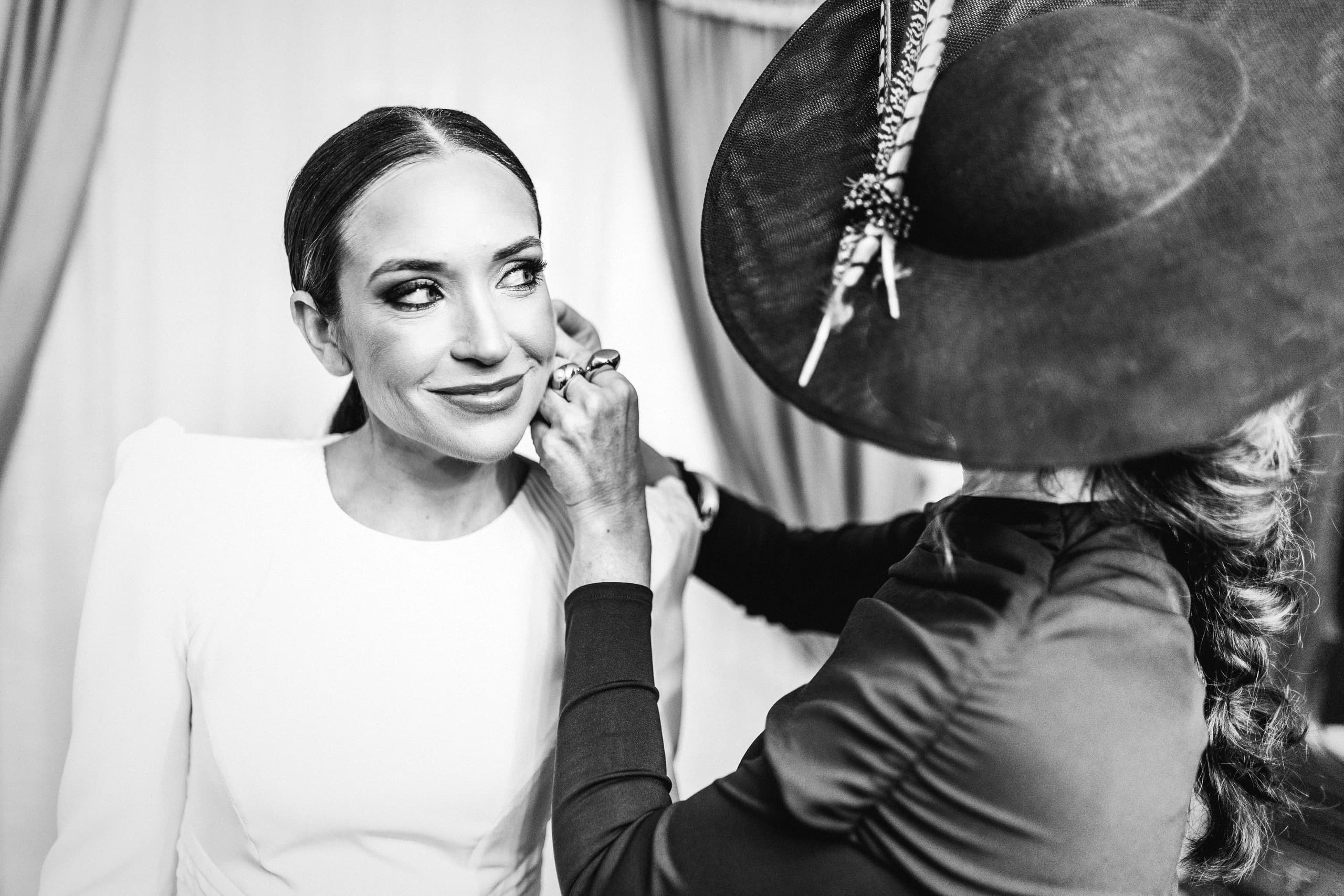 Maquillando a la novia, que sostiene su sombrero, en blanco y negro