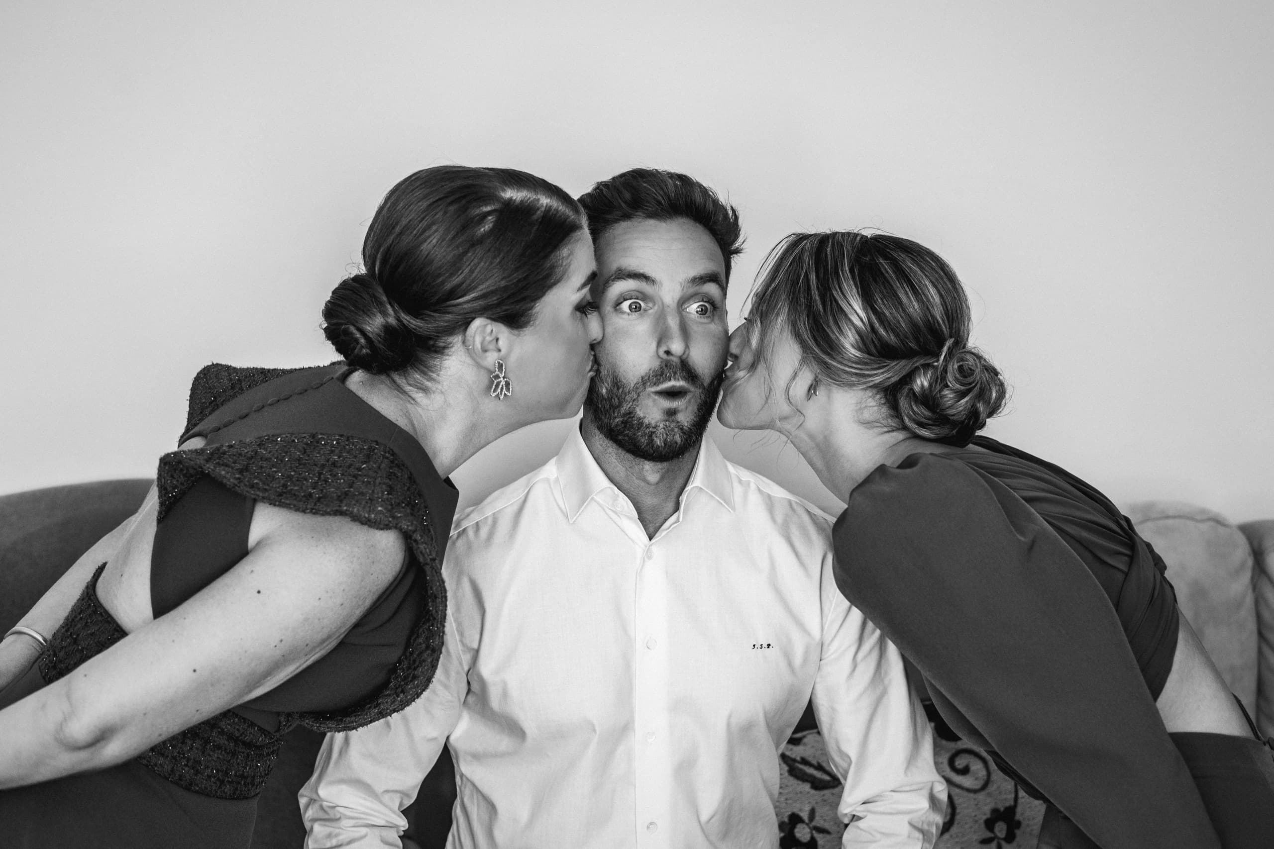 Dos invitadas besando al novio en las mejillas, en blanco y negro