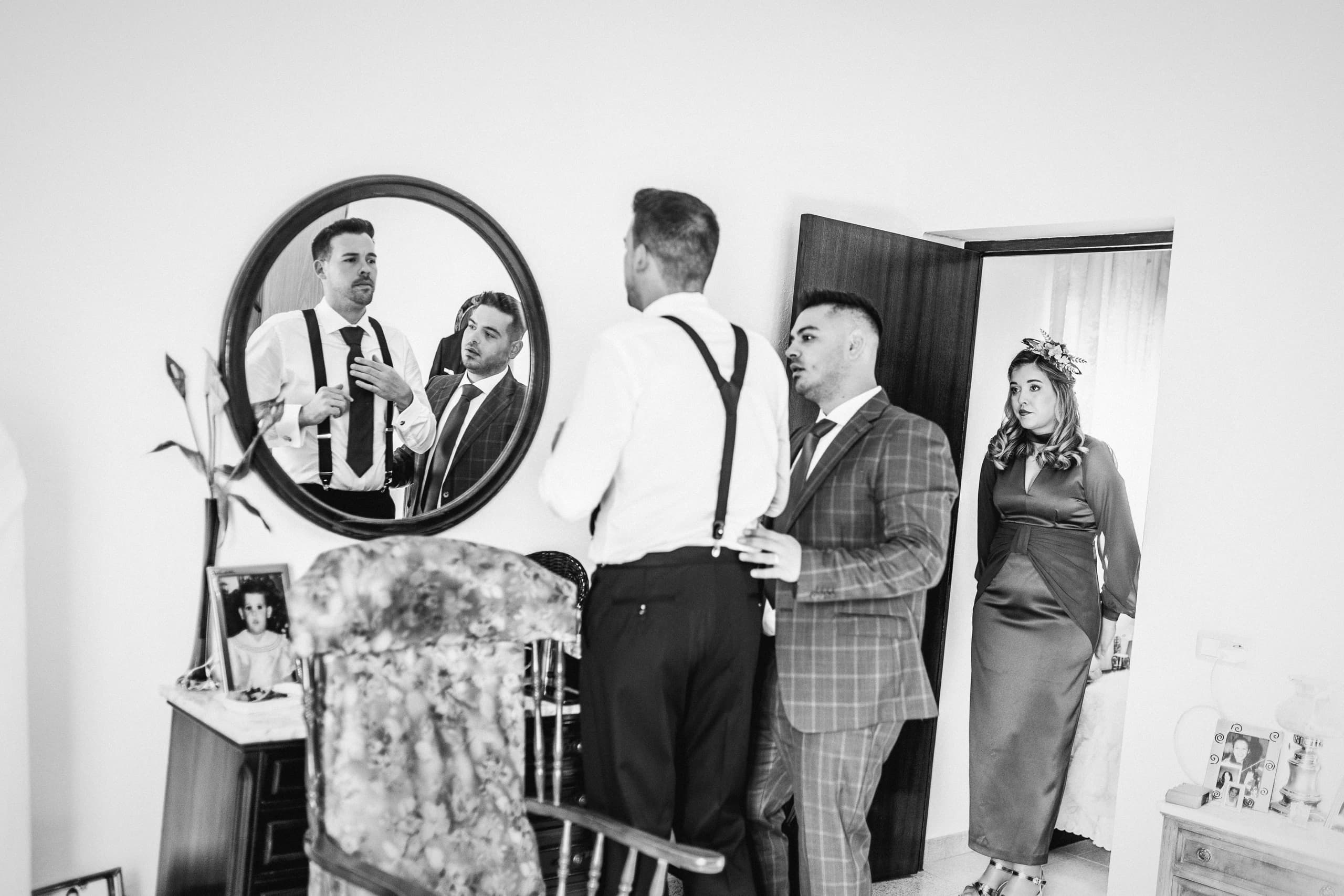 El novio vistiéndose con sus amigos, reflejado en el espejo, en blanco y negro