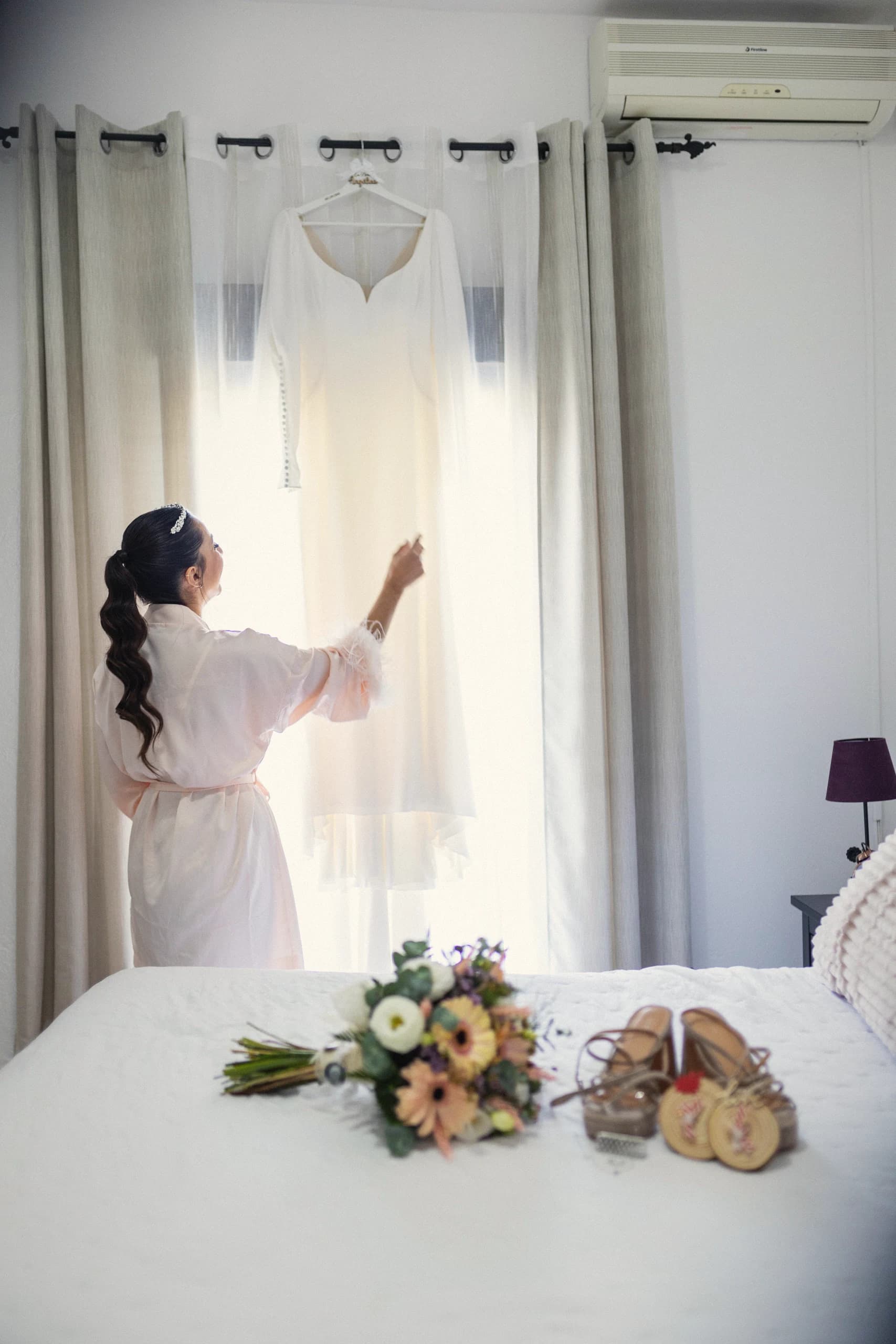 La novia descolgando el vestido junto a la ventana