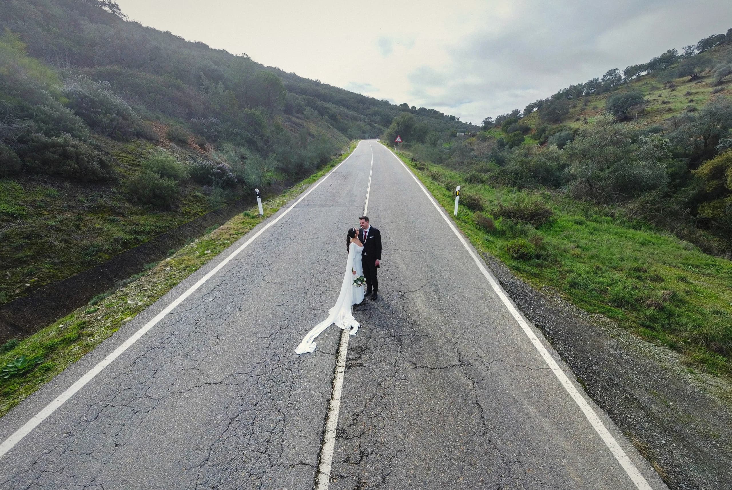 Los novios sobre la carretera con la sierra al fondo, desde el dron