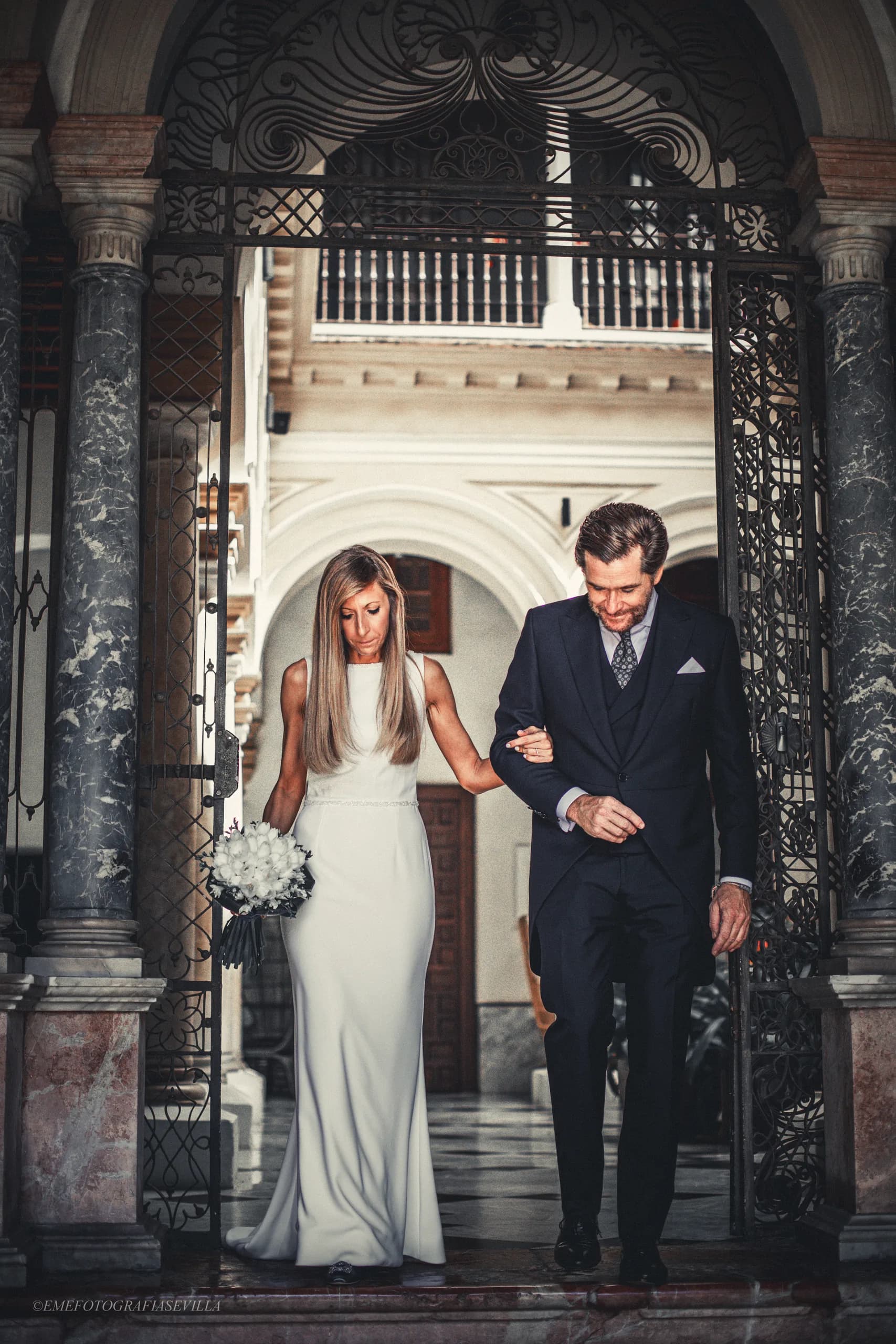 La novia y su padre bajo el portón de rejería, a punto de salir