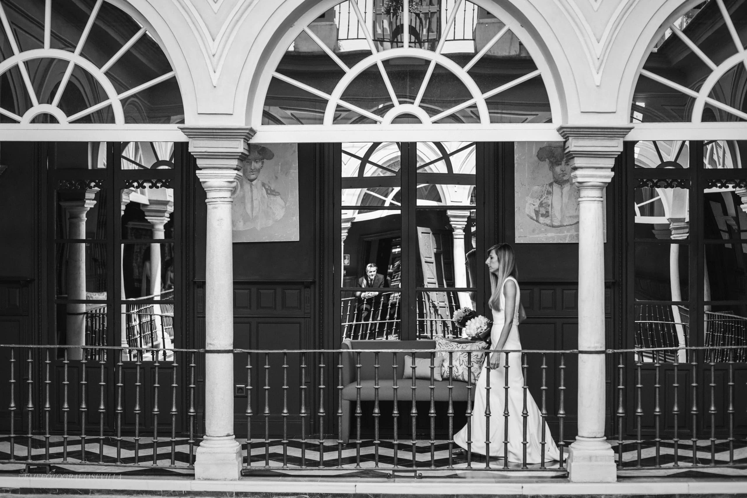 La novia vista desde el otro lado del patio, entre los arcos, en blanco y negro