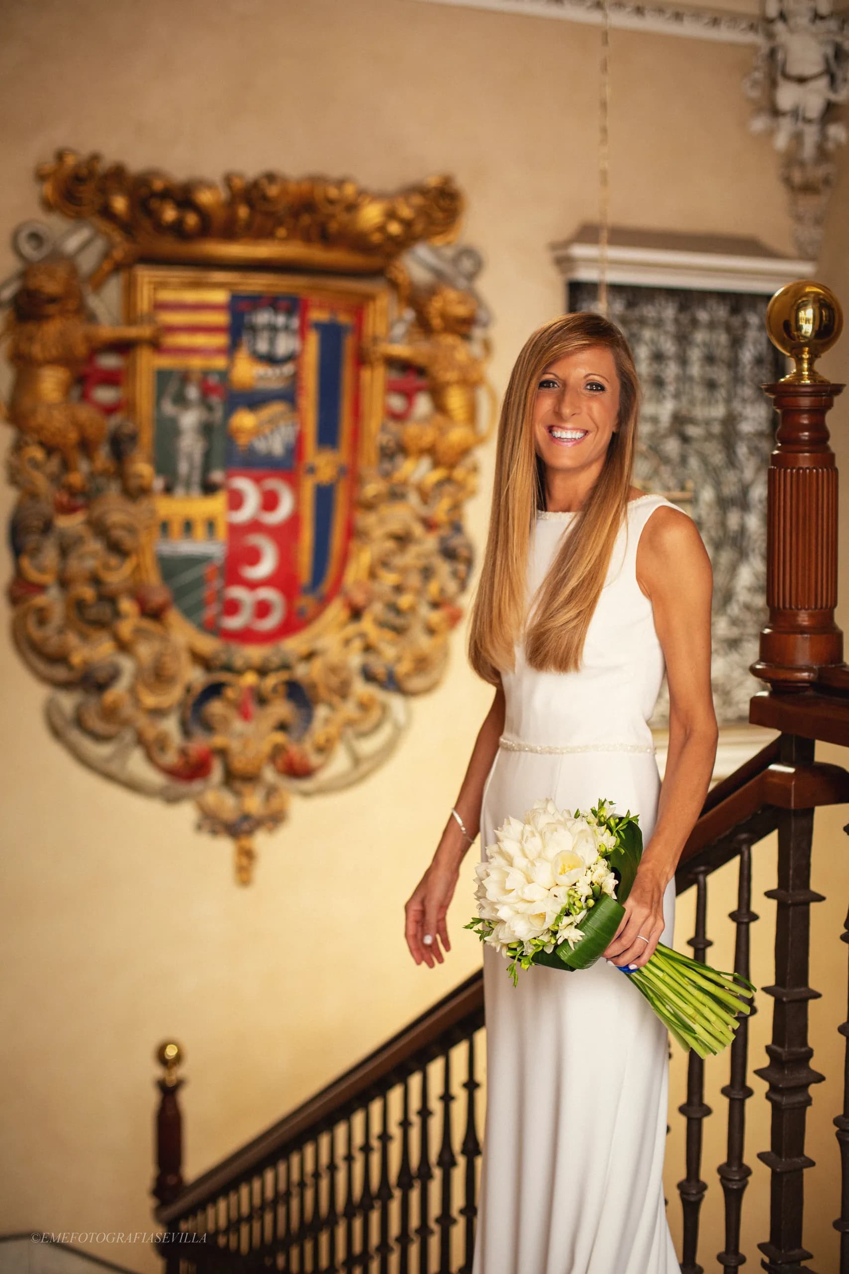 La novia con el ramo en la escalera de la casa, junto al escudo de azulejos