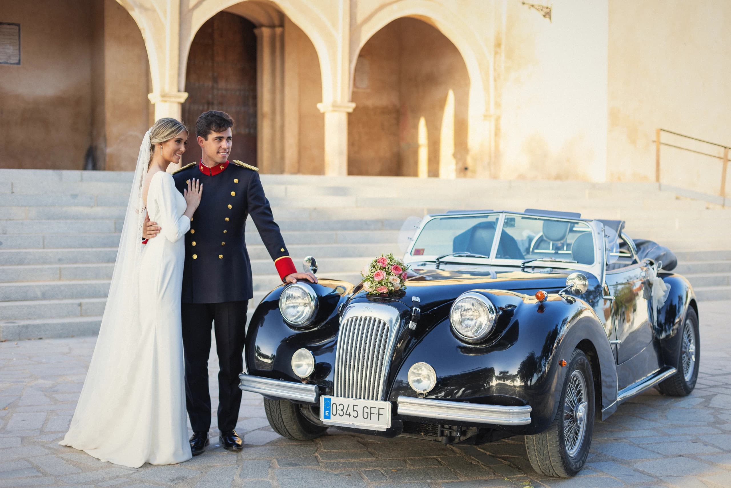 Los novios junto al coche clásico en la plaza de la hacienda