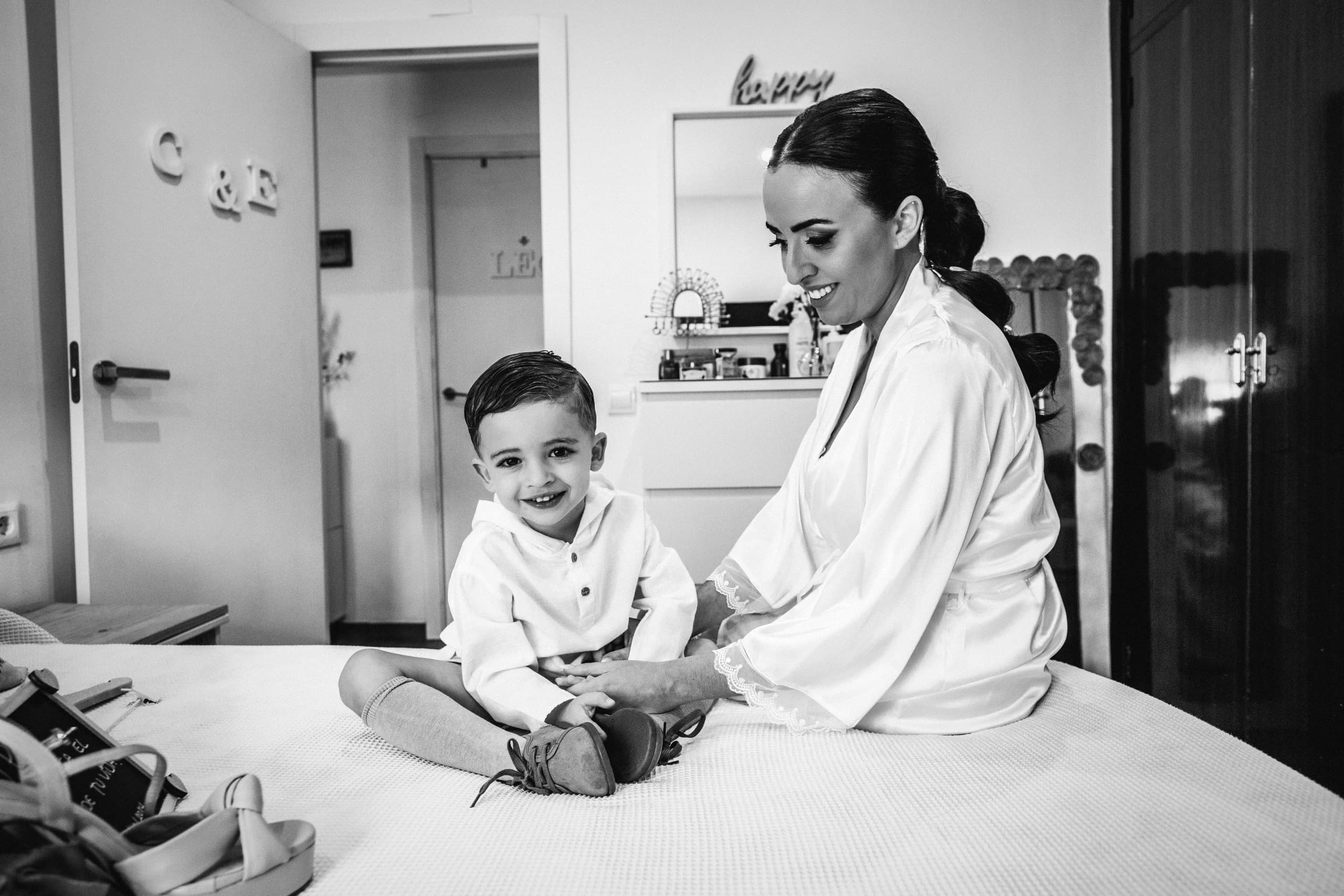 La novia con su hijo sobre la cama antes de vestirse, en blanco y negro