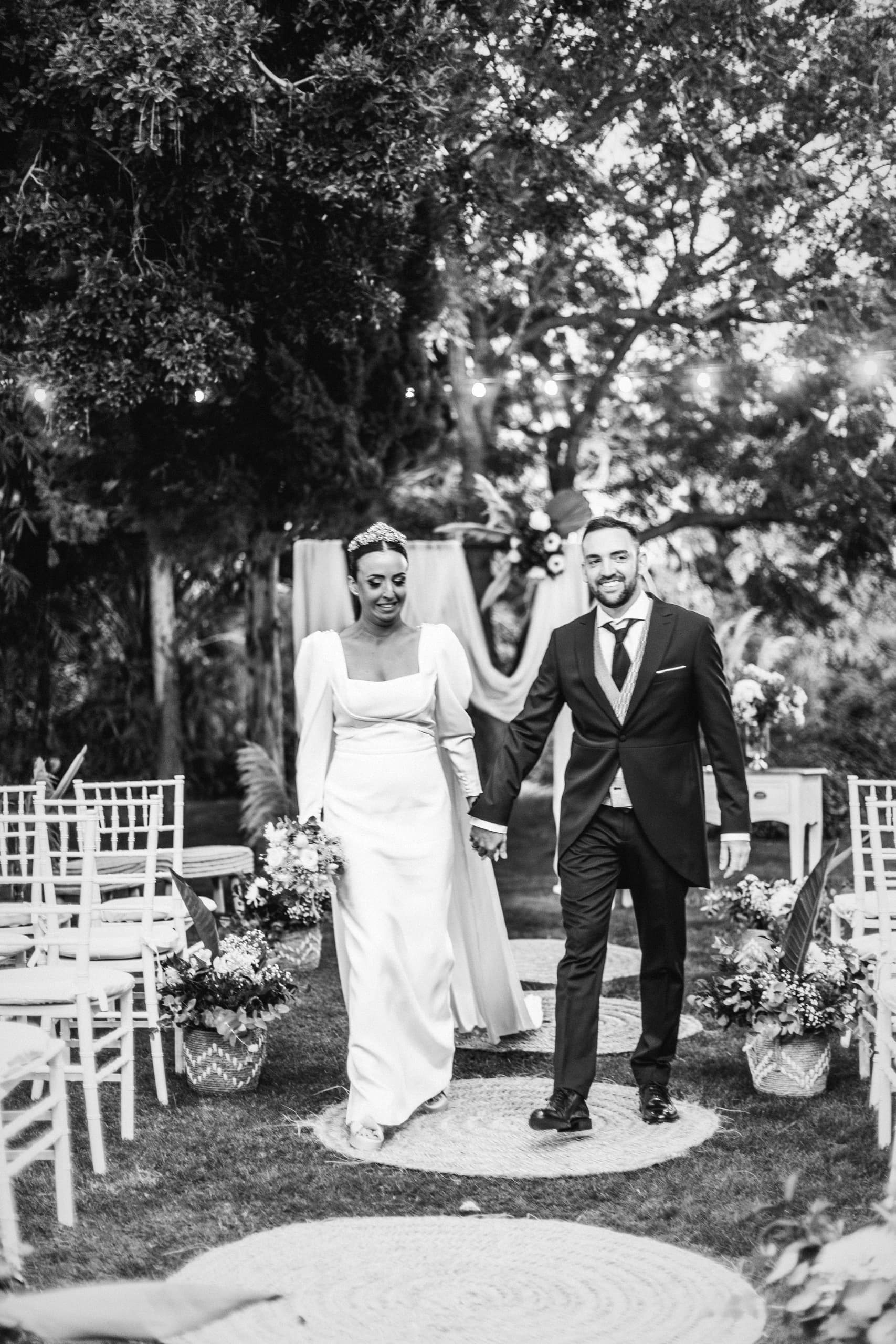Los novios caminando por el pasillo del jardín tras la ceremonia, en blanco y negro