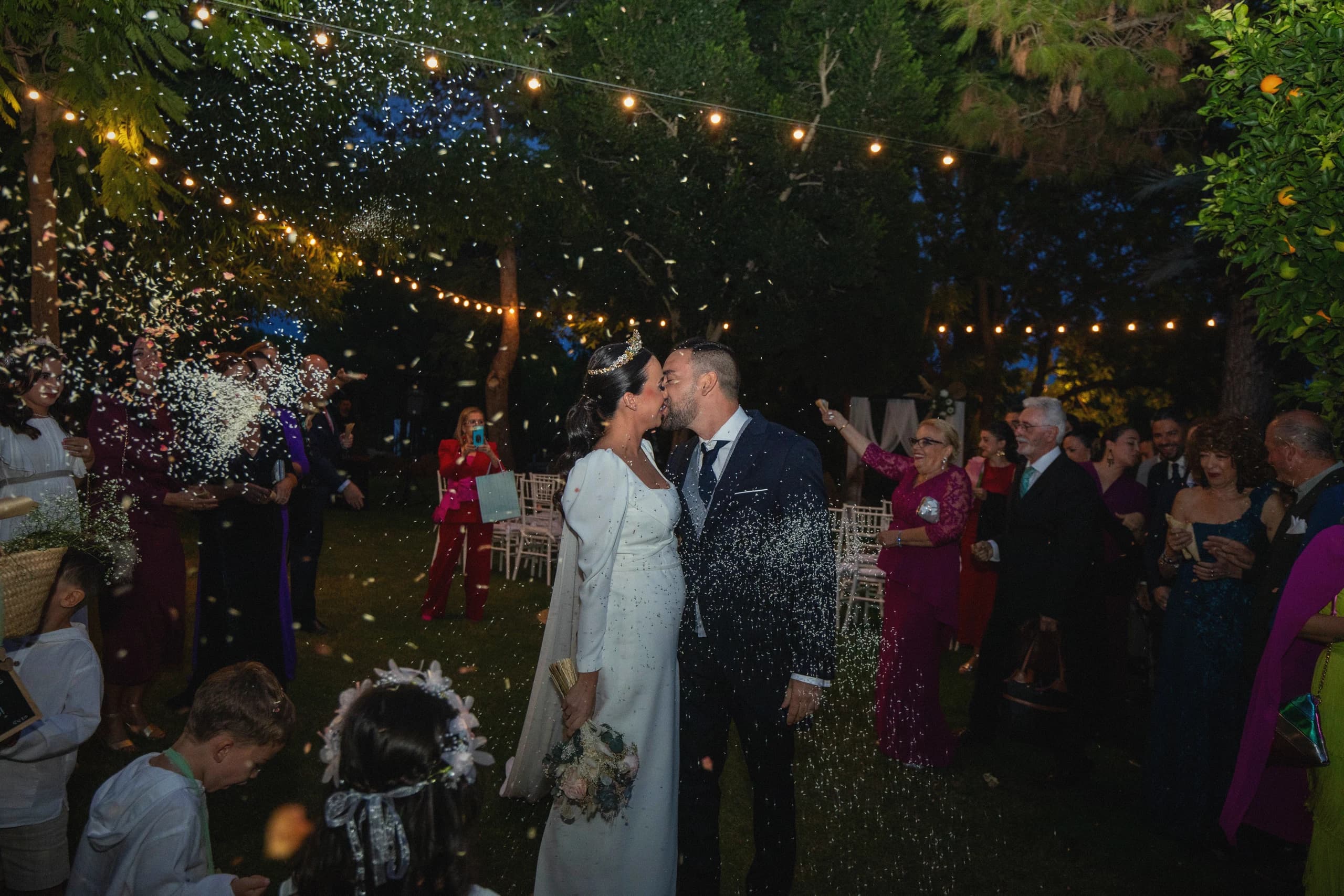Beso entre confeti dorado bajo las luces del jardín