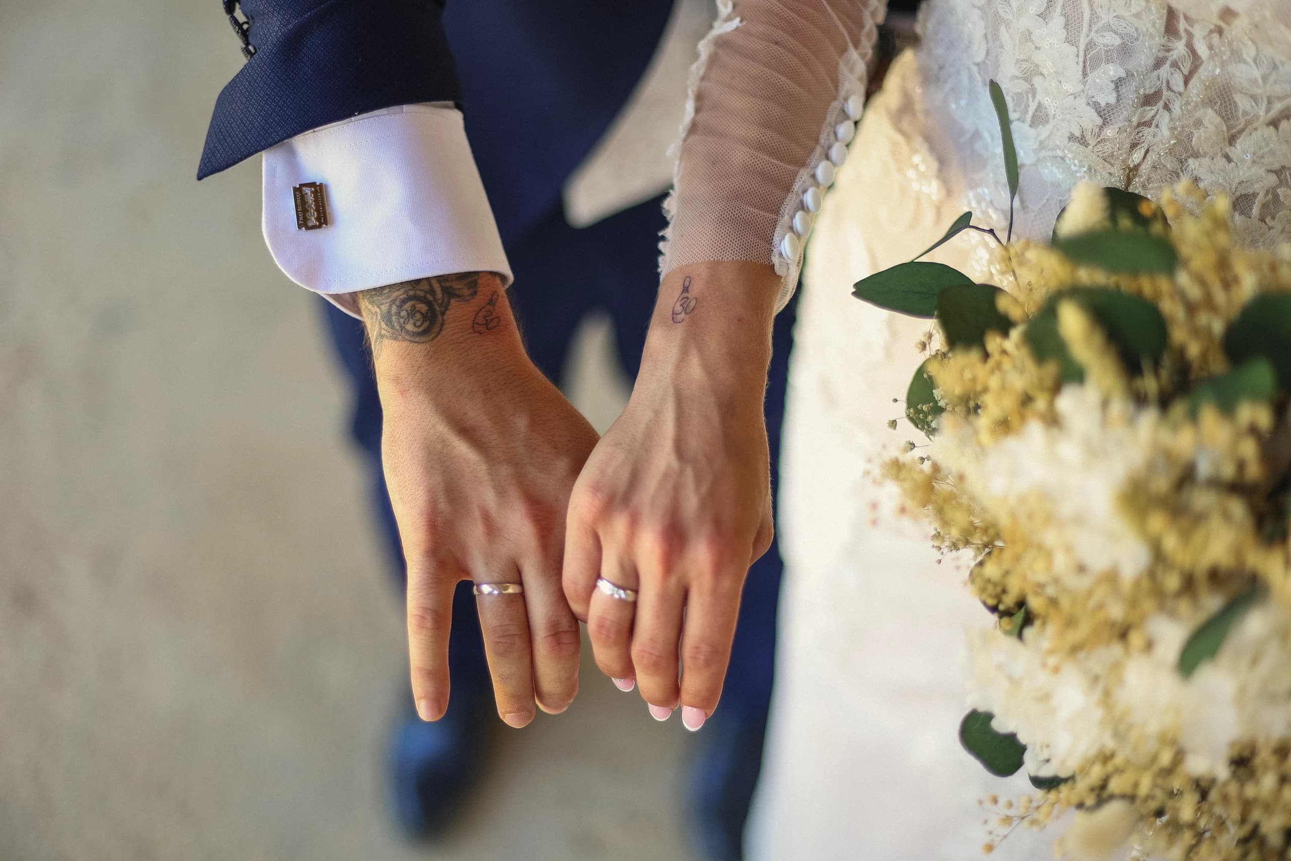 Las manos de los novios con las alianzas, sobre el ramo