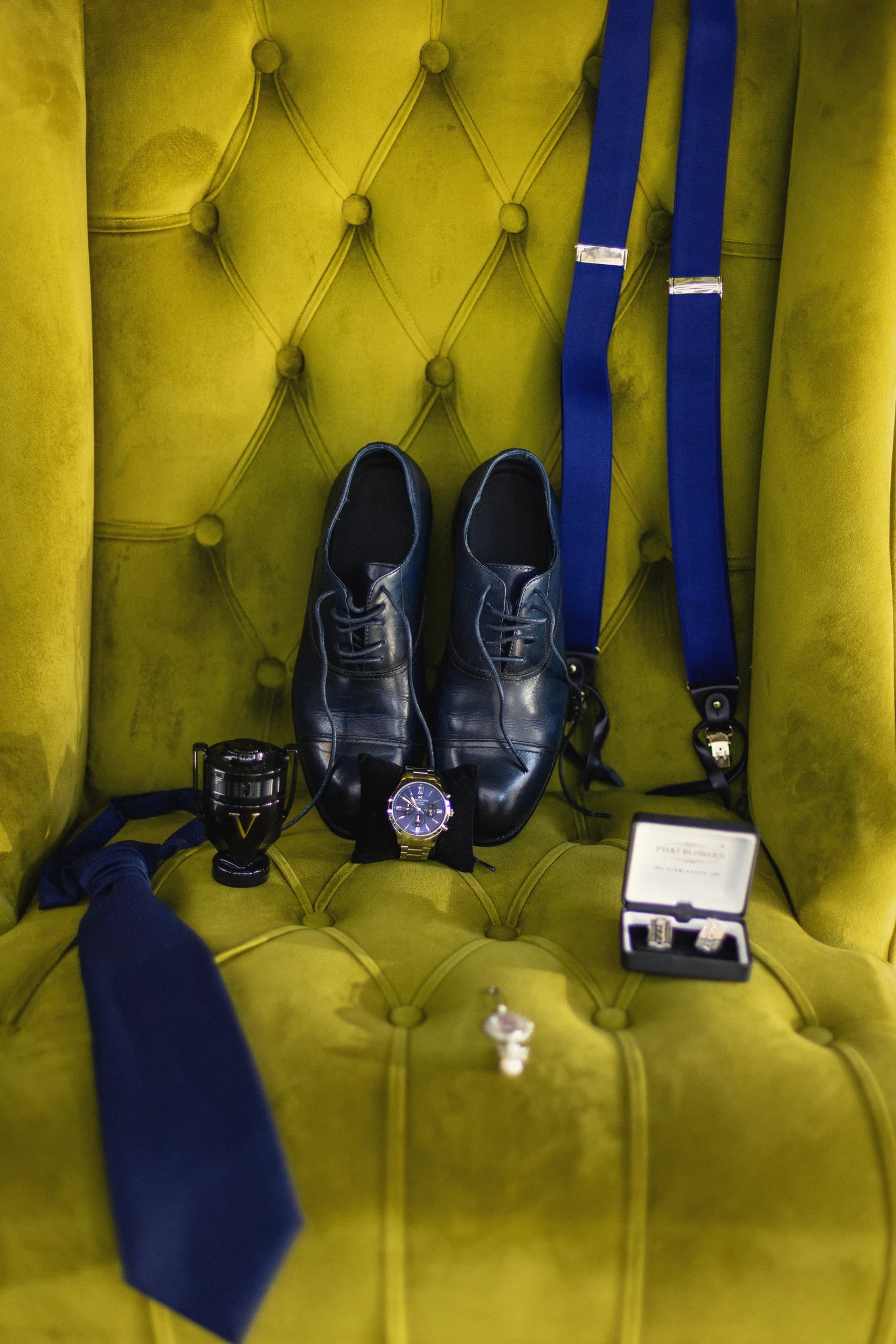 Los zapatos, los tirantes y la corbata del novio sobre el sillón verde