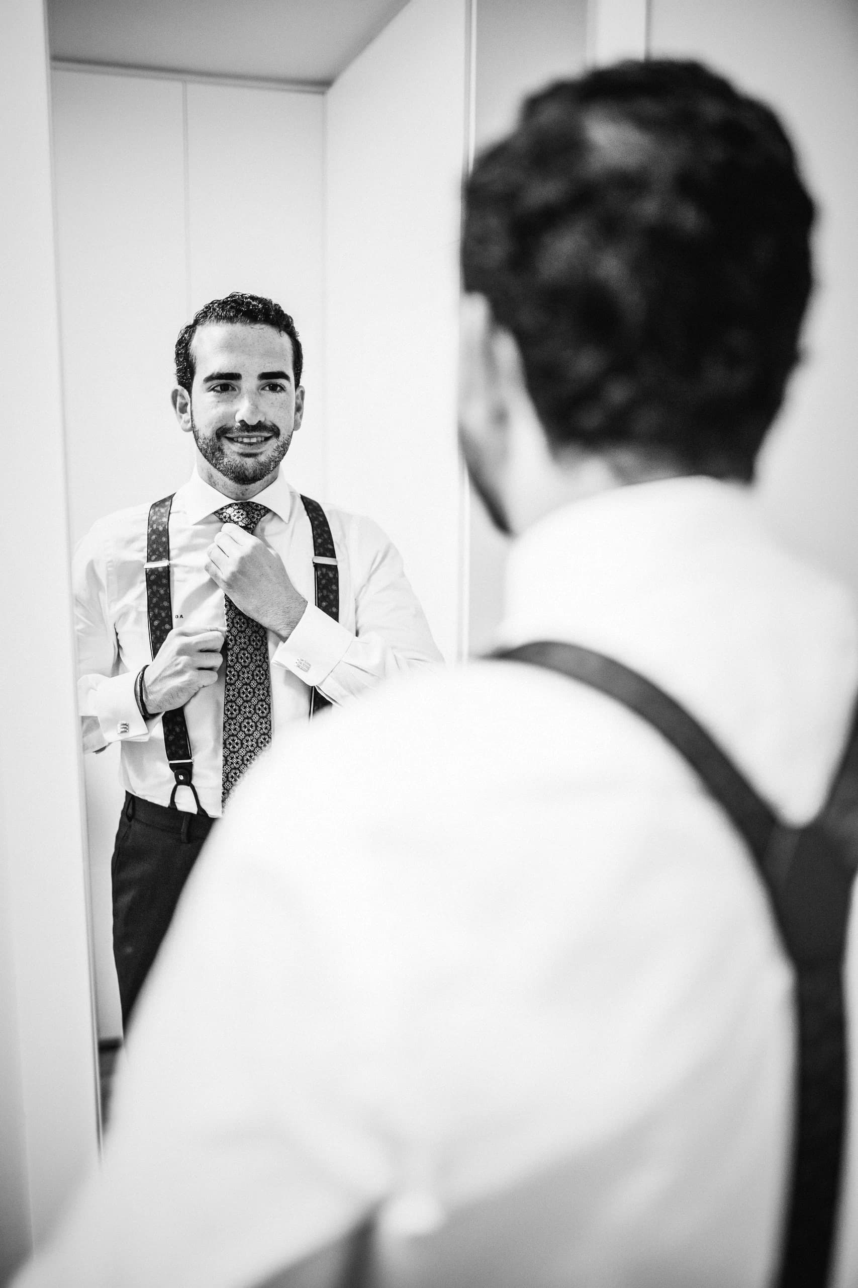 El novio ajustándose la corbata frente al espejo, en blanco y negro