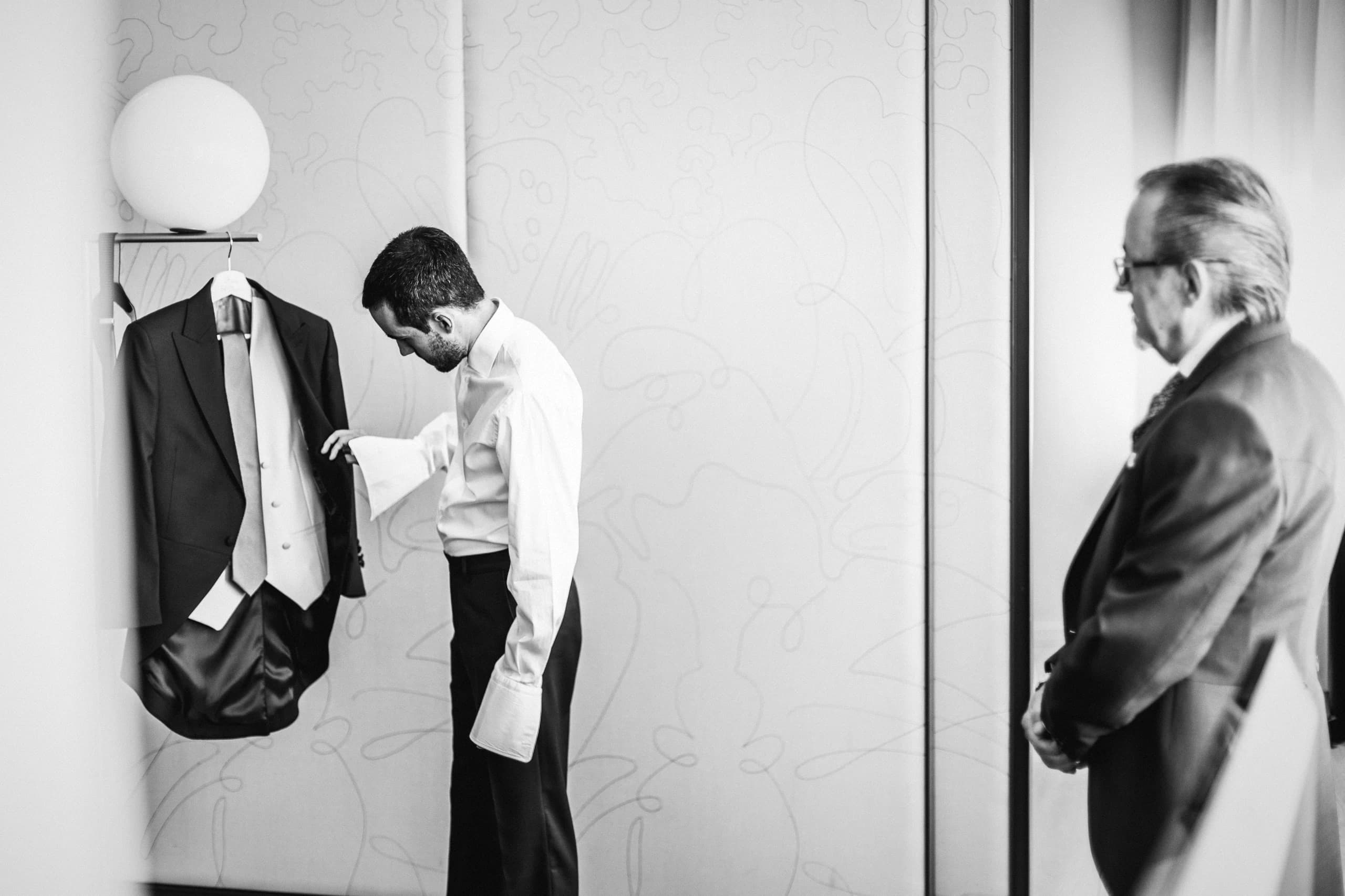 El novio vistiéndose mientras su padre lo espera en el descansillo, en blanco y negro
