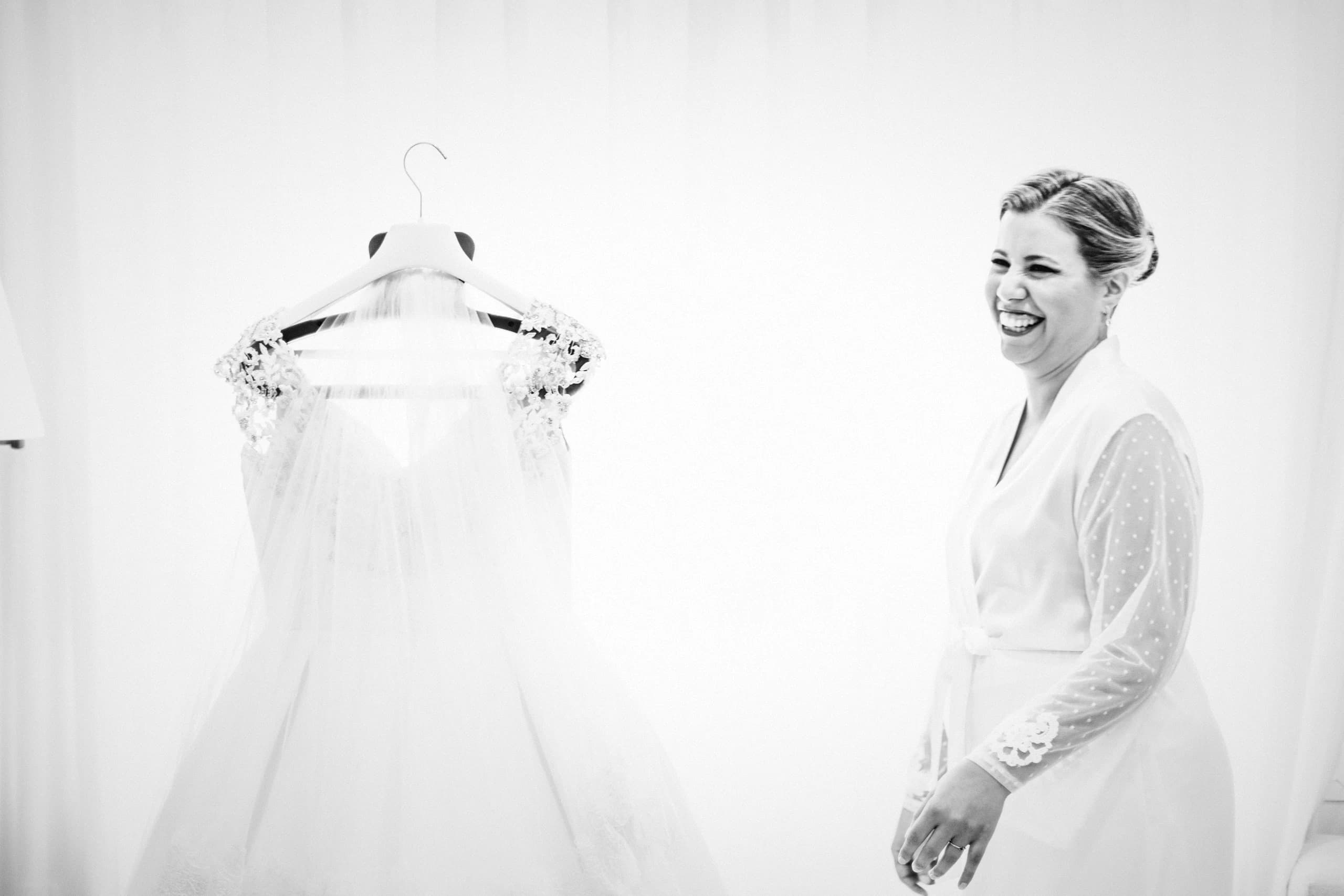 La novia riéndose junto al vestido todavía colgado de la percha