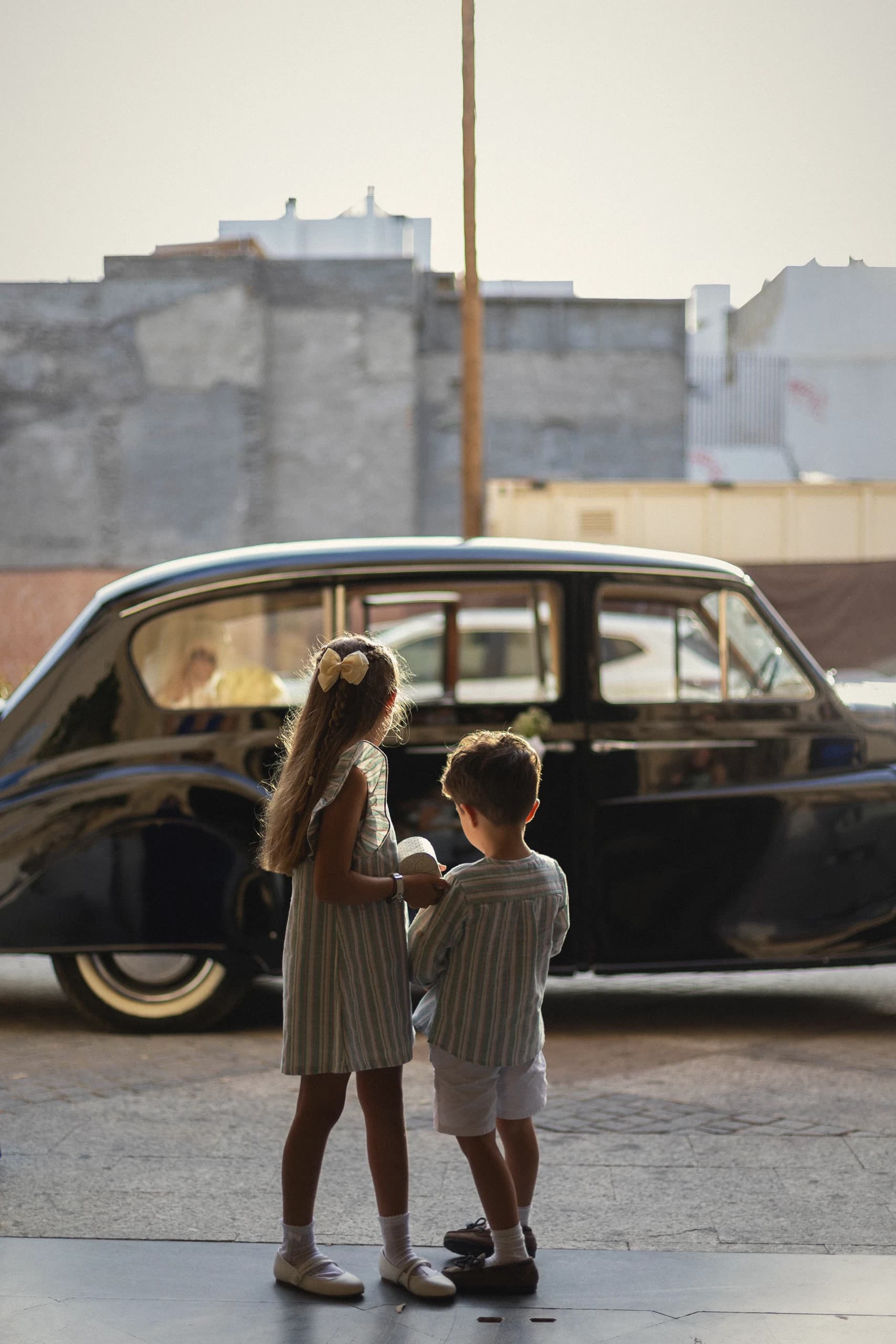 Dos niños esperando junto al coche clásico en mitad de la calle