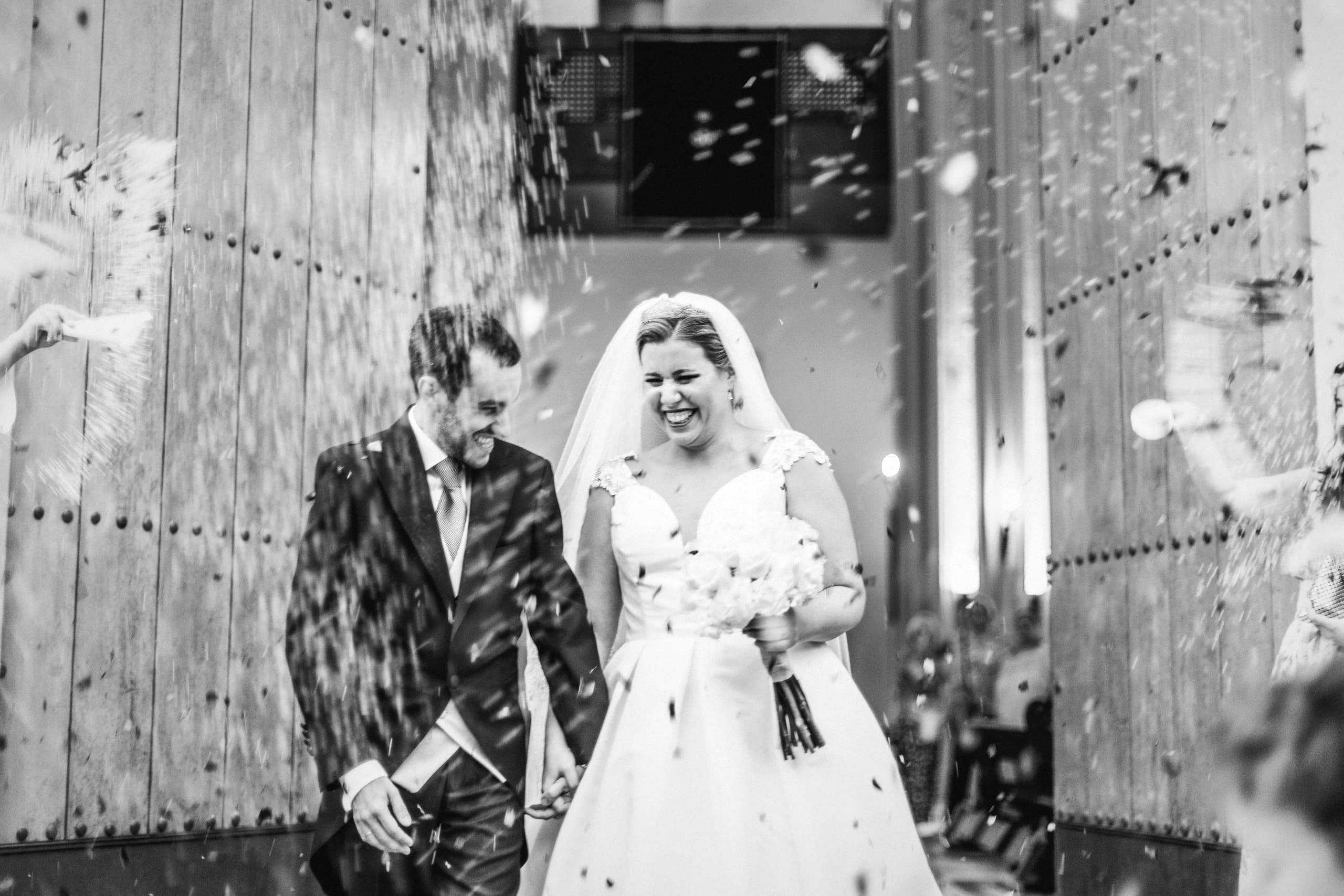 Los novios saliendo por el portón de la iglesia bajo el arroz, en blanco y negro