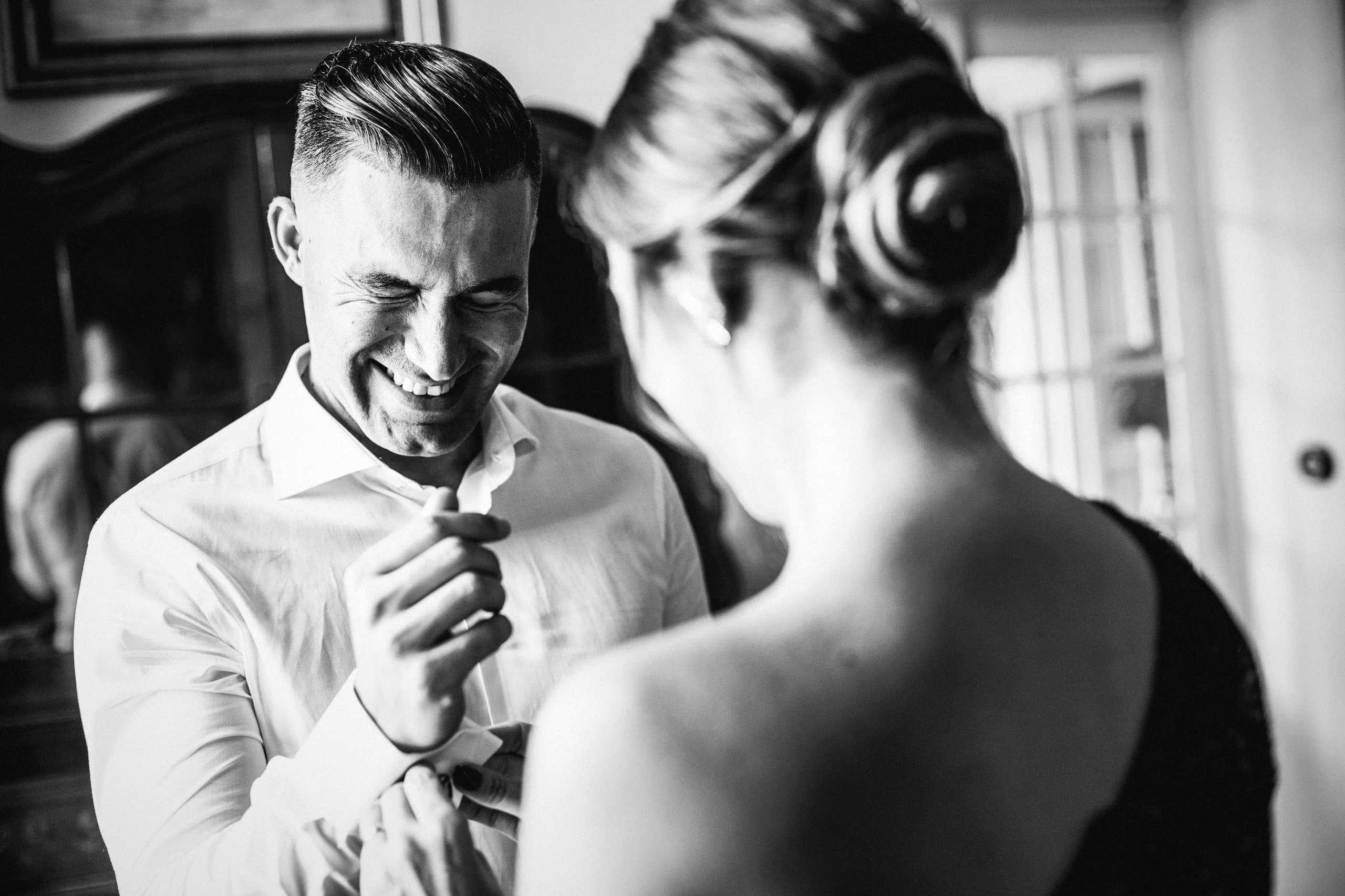 El novio riendo mientras le arreglan la camisa, en blanco y negro