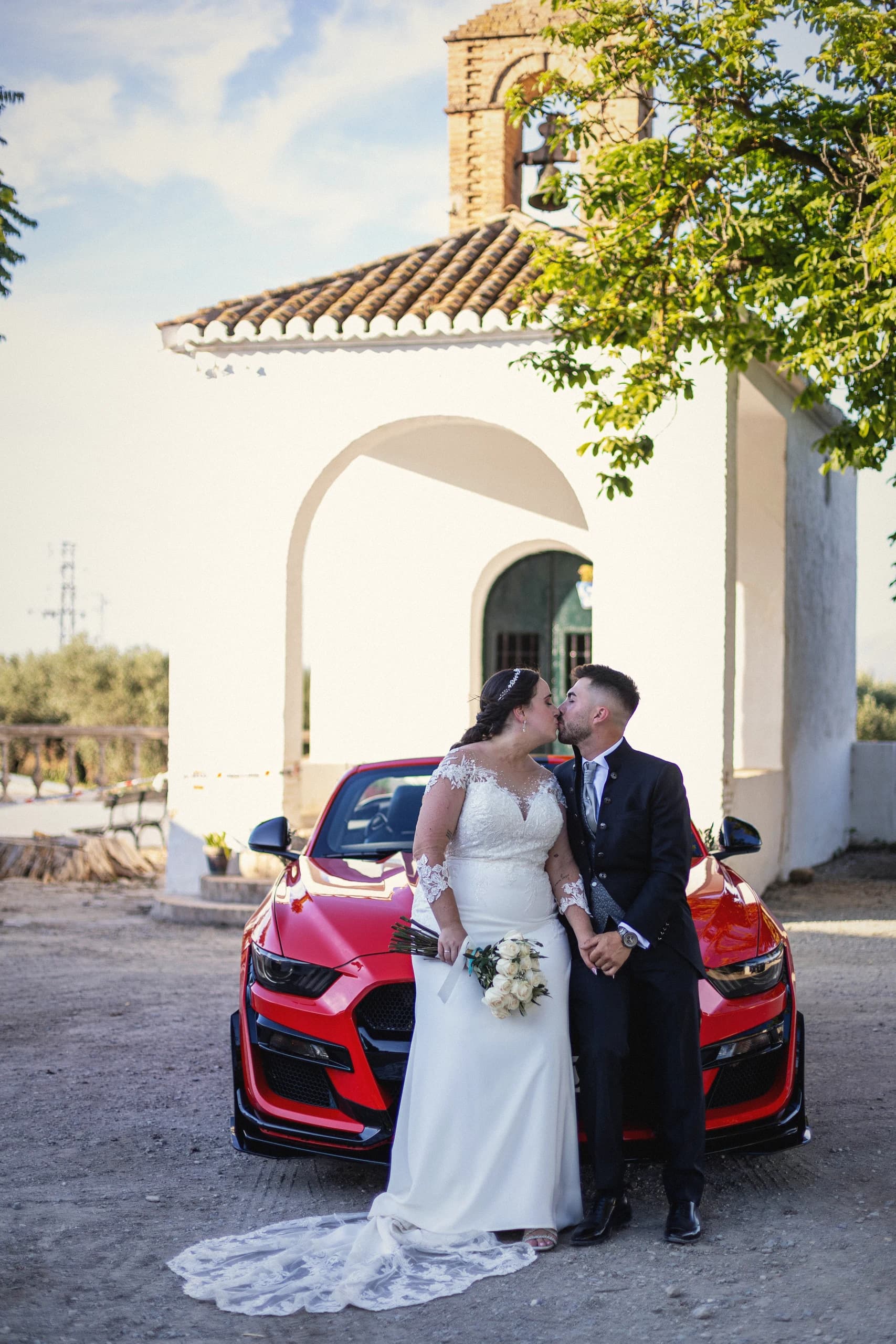 Beso junto al Mustang rojo con la ermita detrás