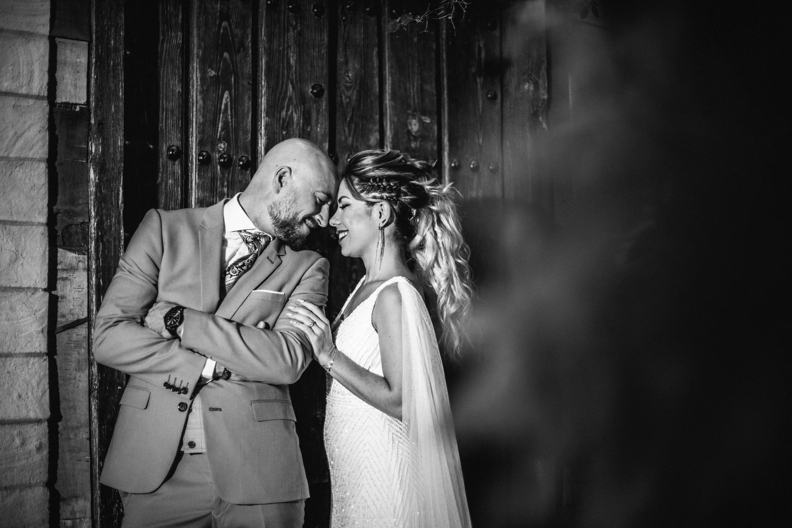 Los novios ante el portón de madera, en blanco y negro