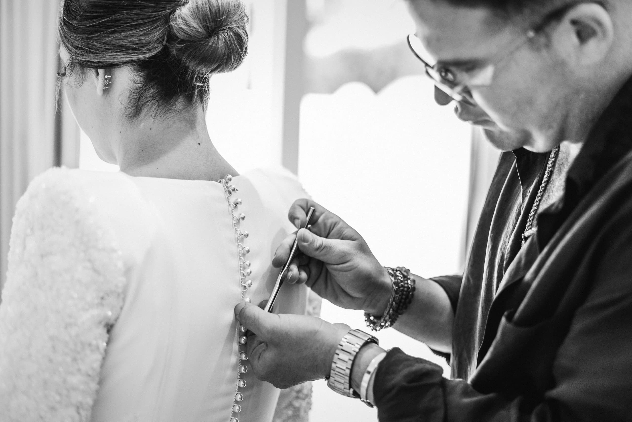 Abrochándole el vestido a la novia junto a la ventana