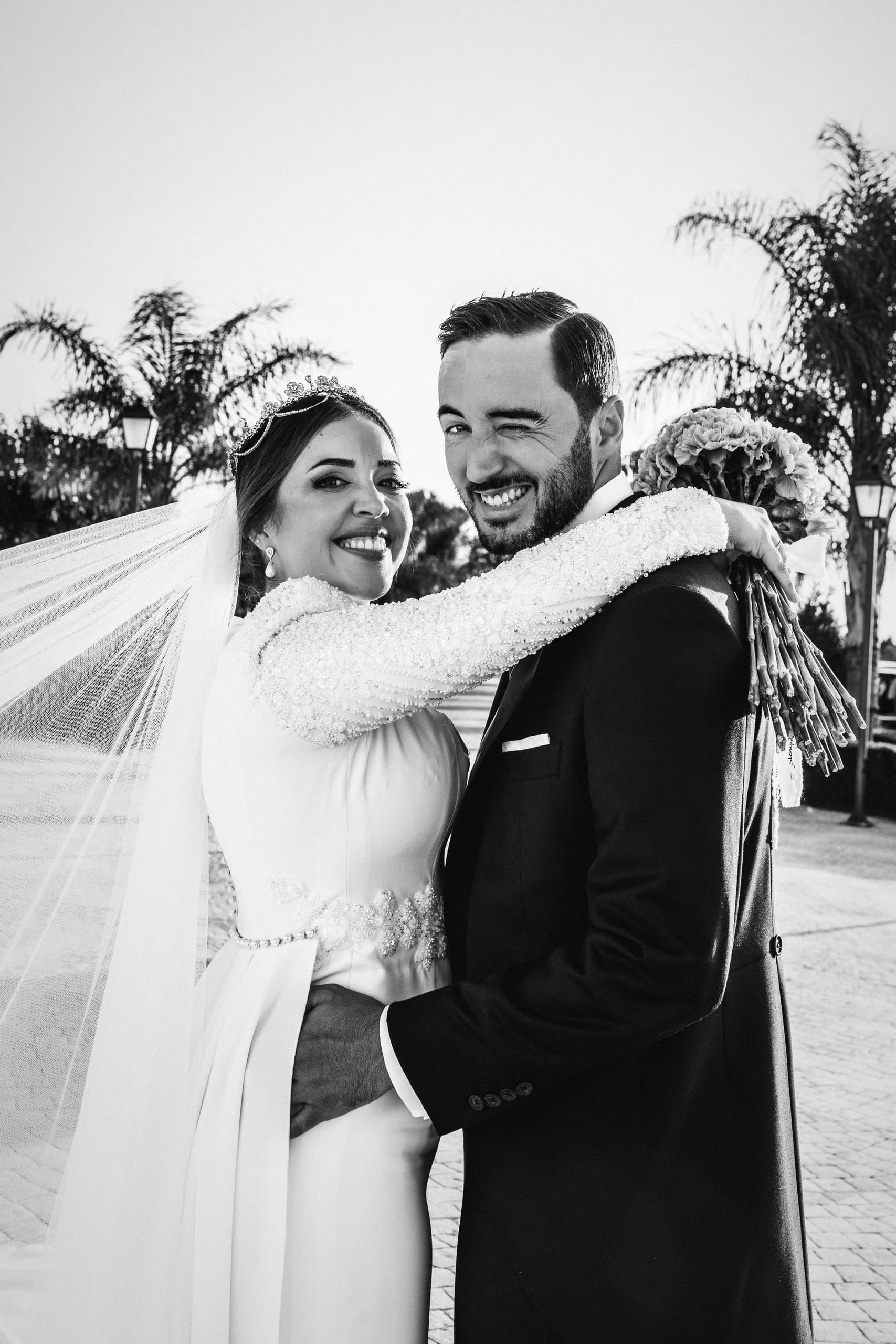 Los novios abrazados, ella con el velo al viento, en blanco y negro