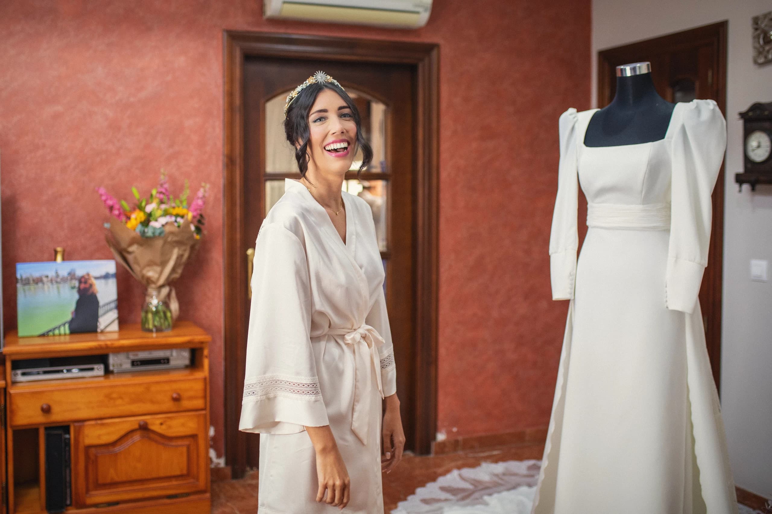 La novia con la bata mirando su vestido en el maniquí