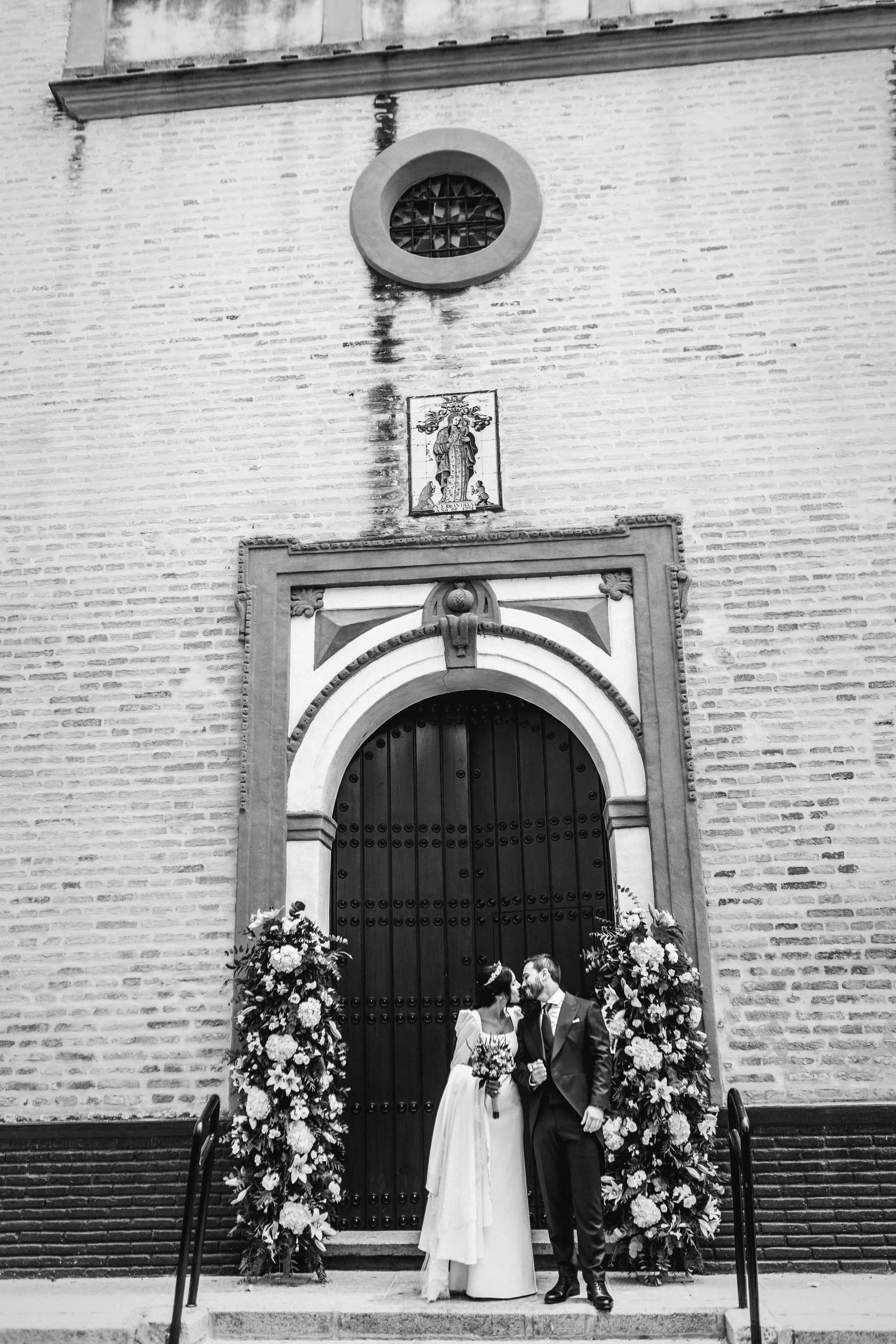 Los novios bajo el arco de la puerta de la iglesia, en blanco y negro