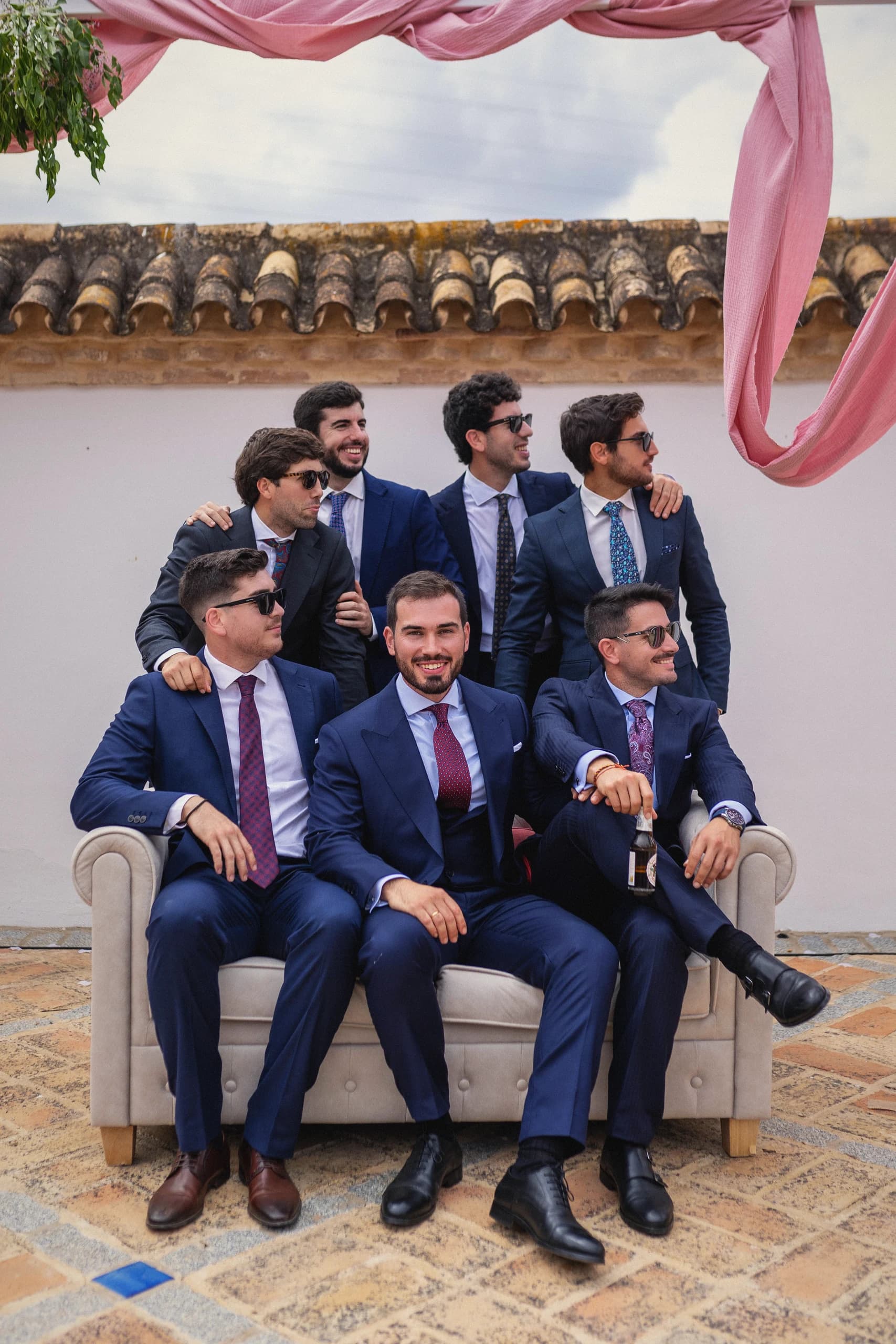 El novio con sus amigos en el sofá bajo las telas rosas