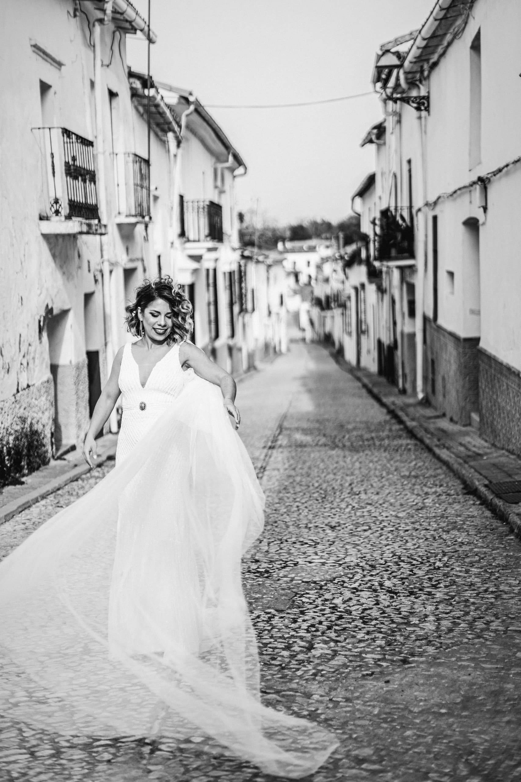 La novia con el velo al viento en la calle empedrada, en blanco y negro