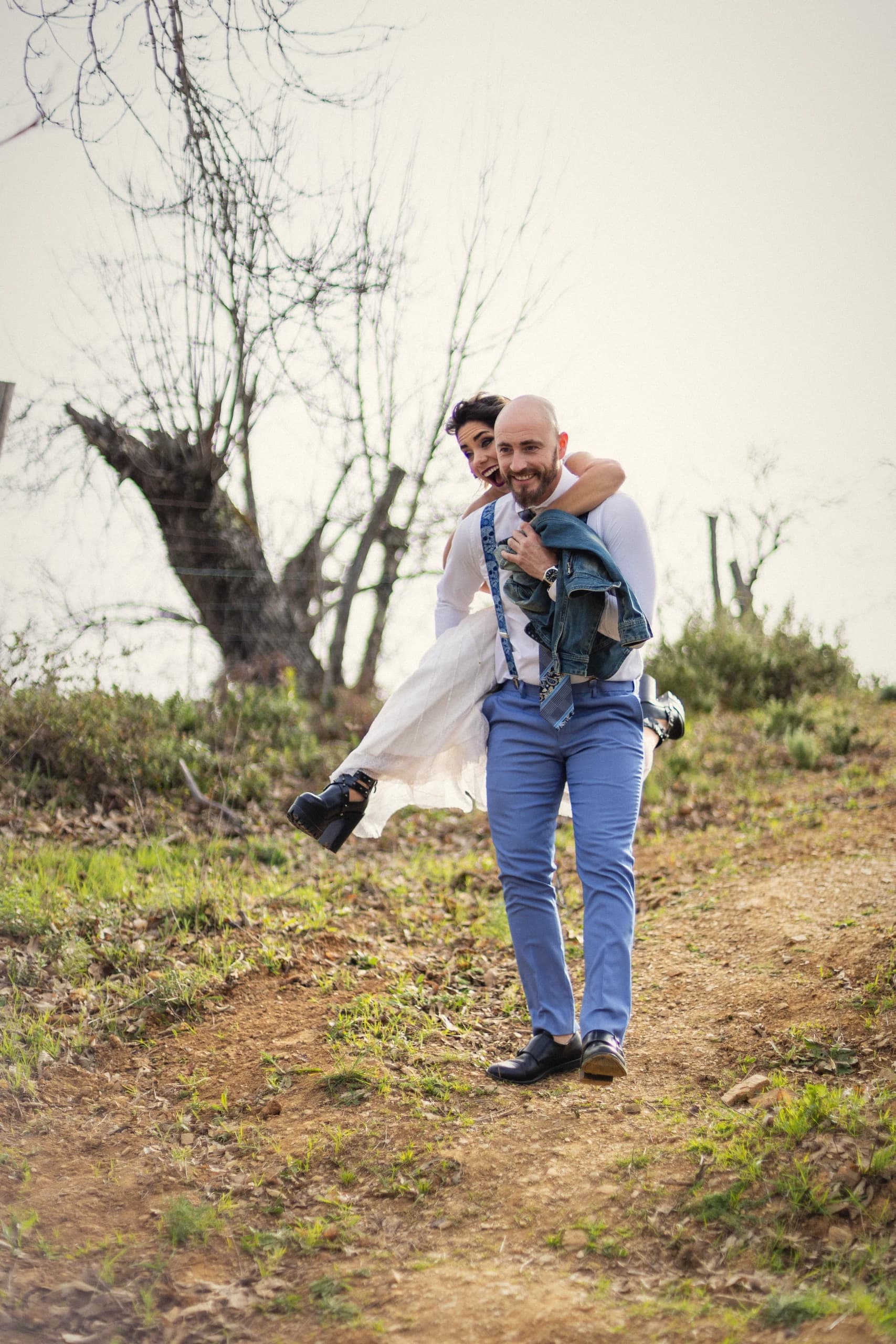 El novio cargando a la novia al hombro por un camino de tierra