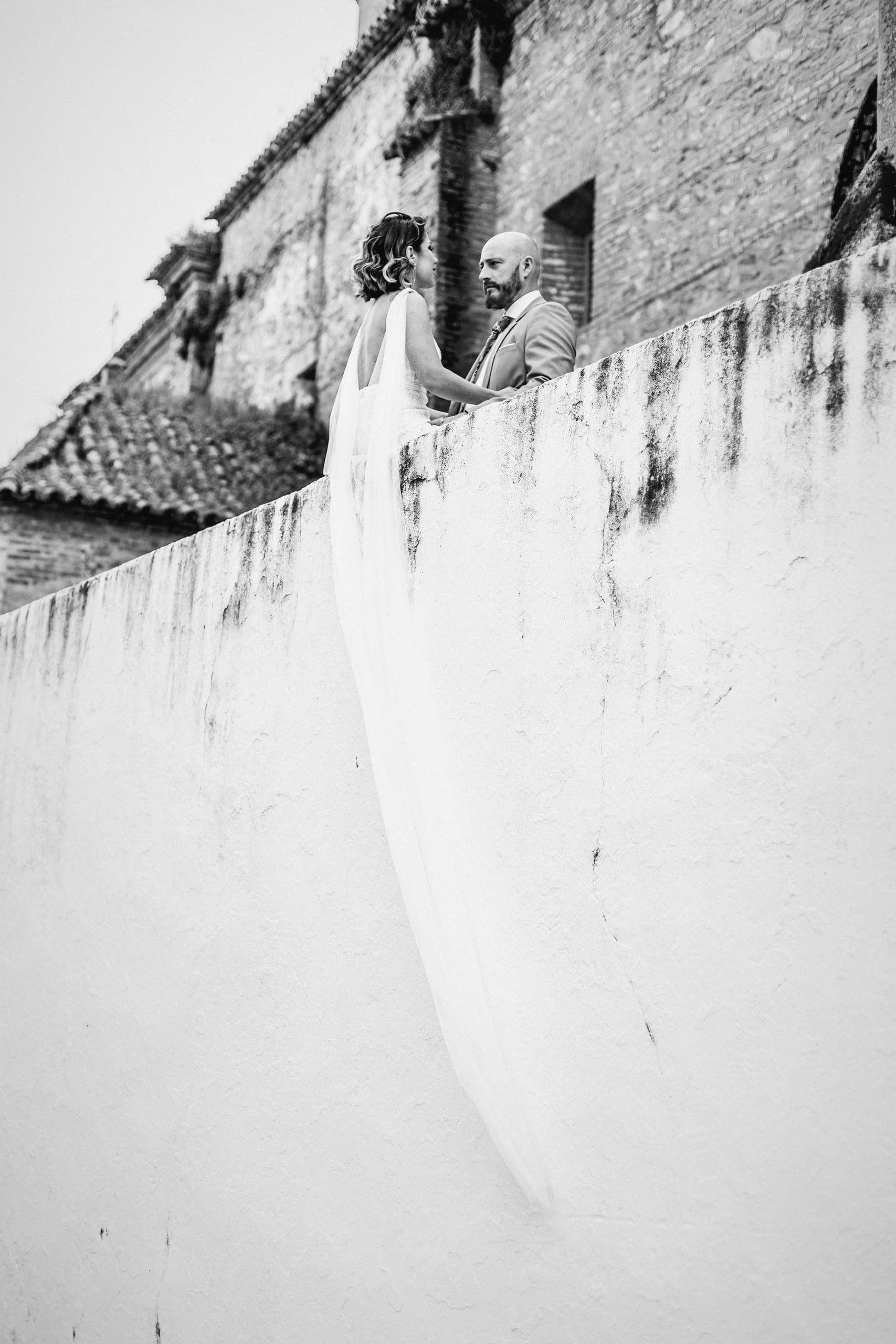 El velo barriendo la pared encalada mientras él asoma por encima del muro, en blanco y negro