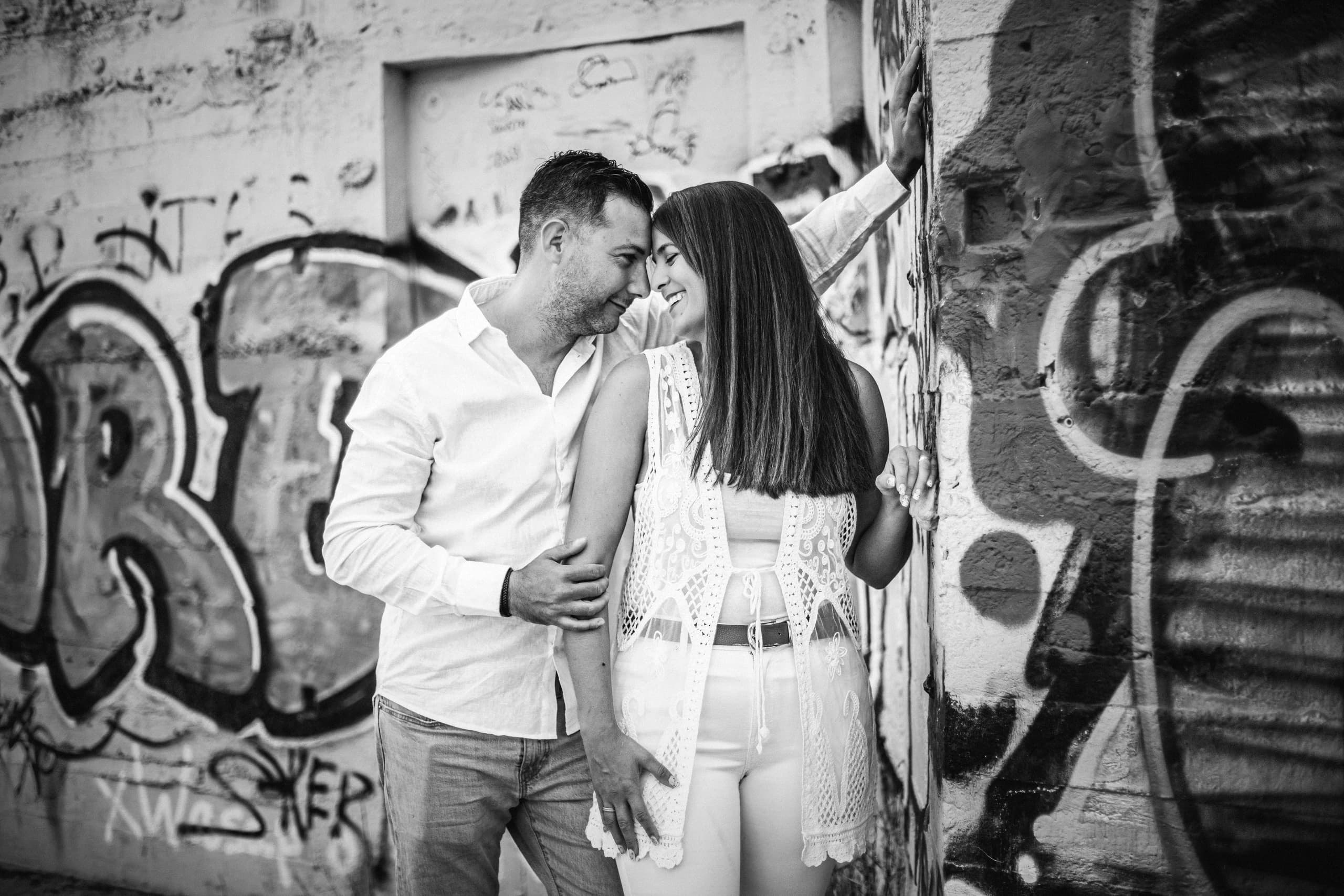 La pareja frente a frente junto a un muro pintado, en blanco y negro