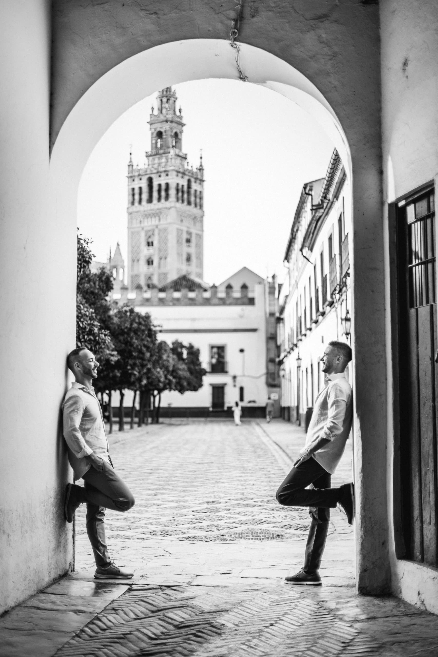 Apoyados a cada lado del arco del Patio de Banderas, con la Giralda al fondo, en blanco y negro