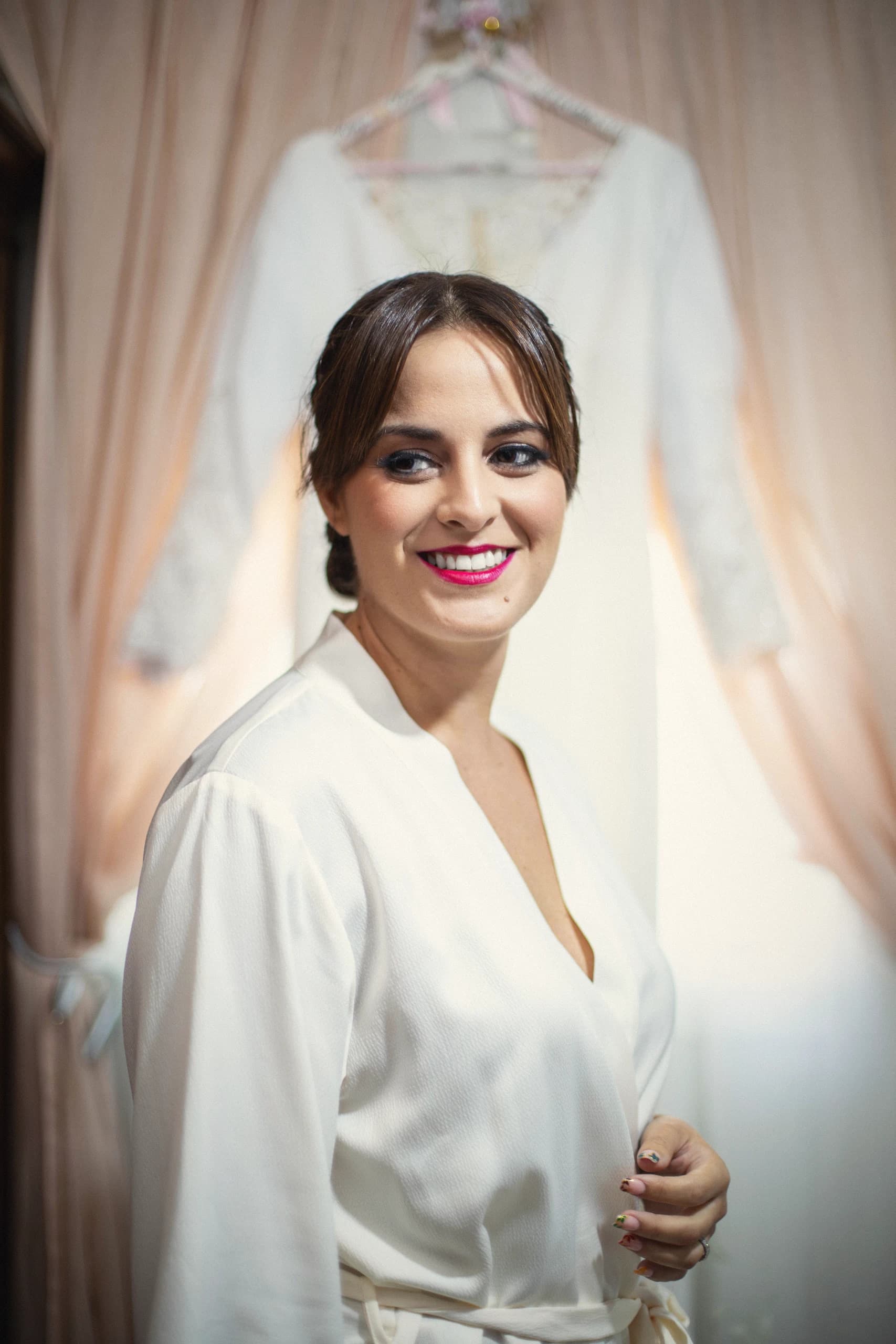 La novia con la bata junto a la ventana, con el vestido colgado detrás