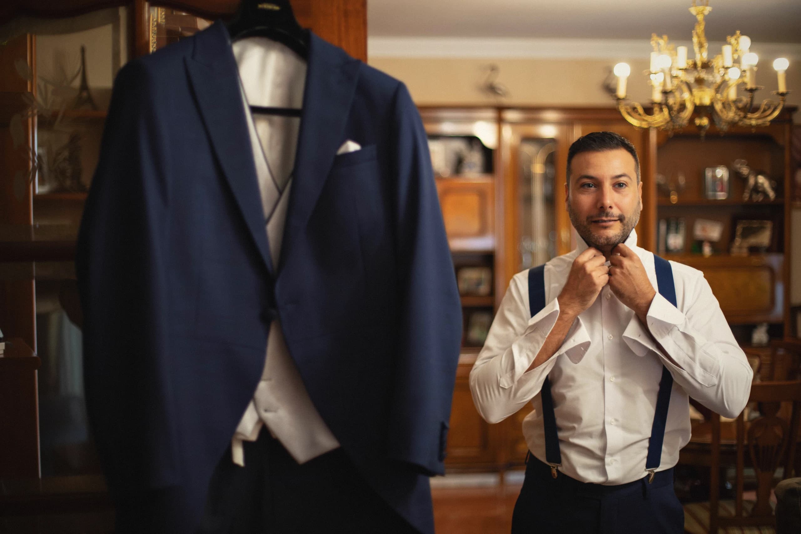 El novio con los tirantes junto al traje colgado