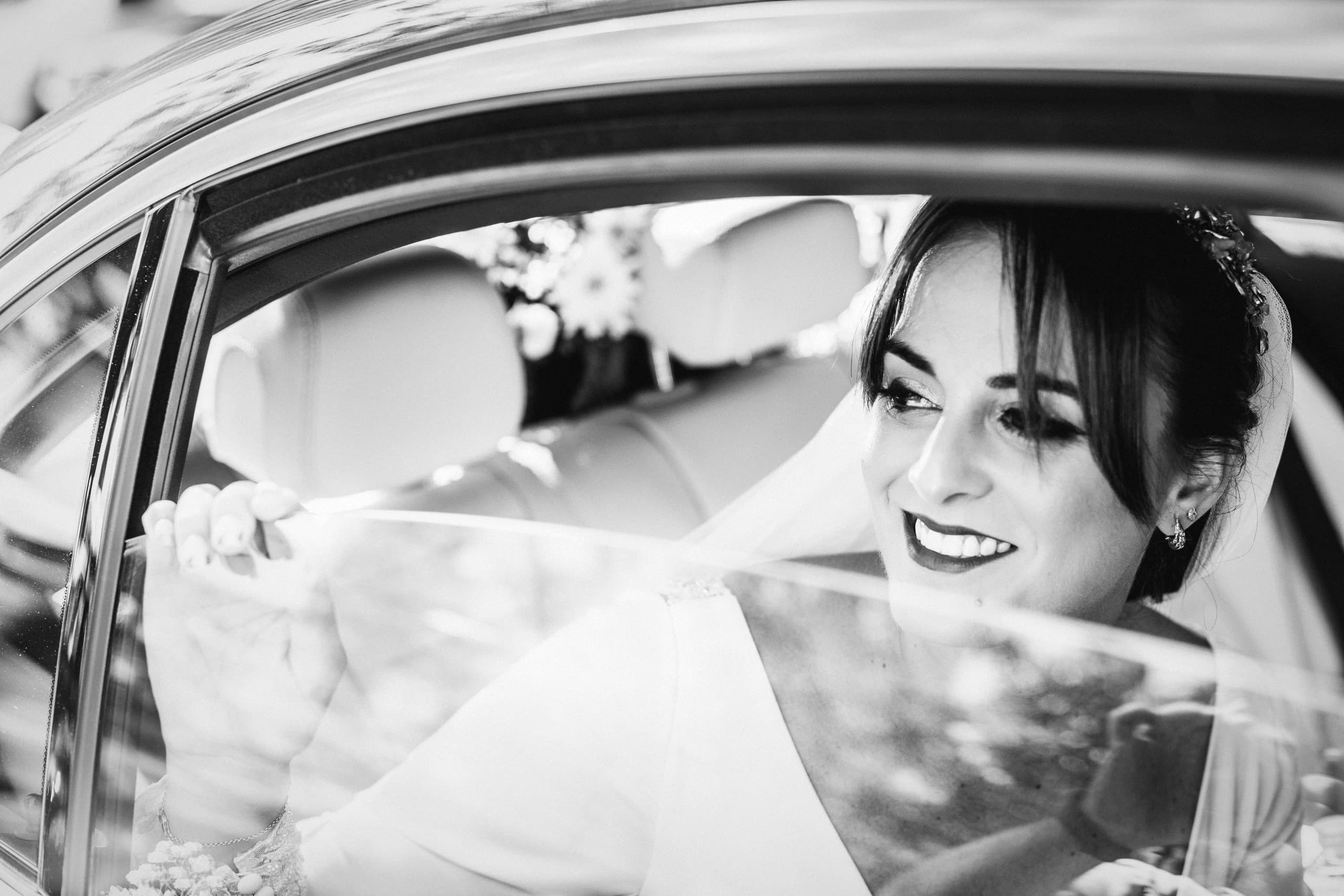 La novia sonriendo desde el coche, en blanco y negro