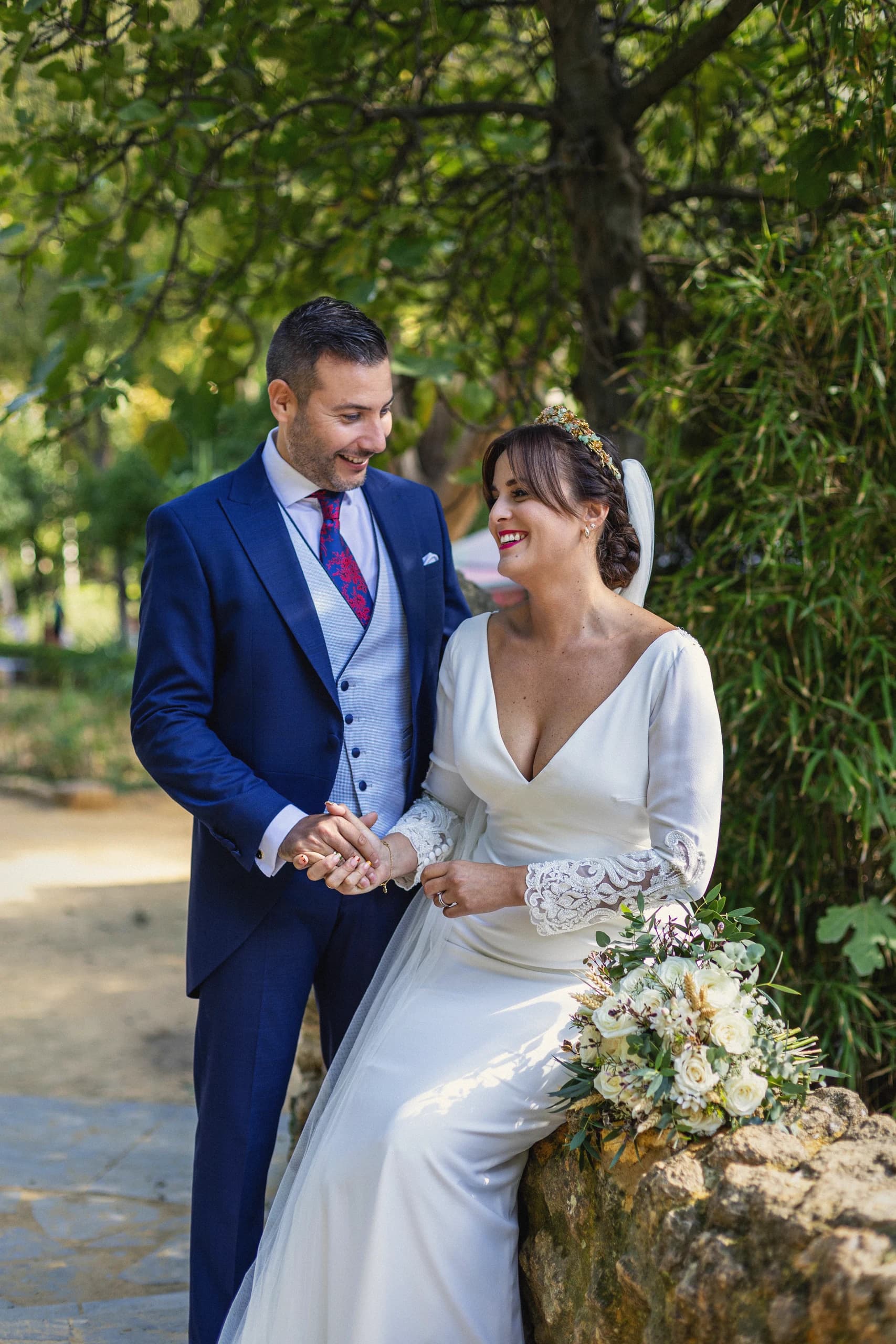 Los novios de la mano junto al muro de piedra, con el ramo