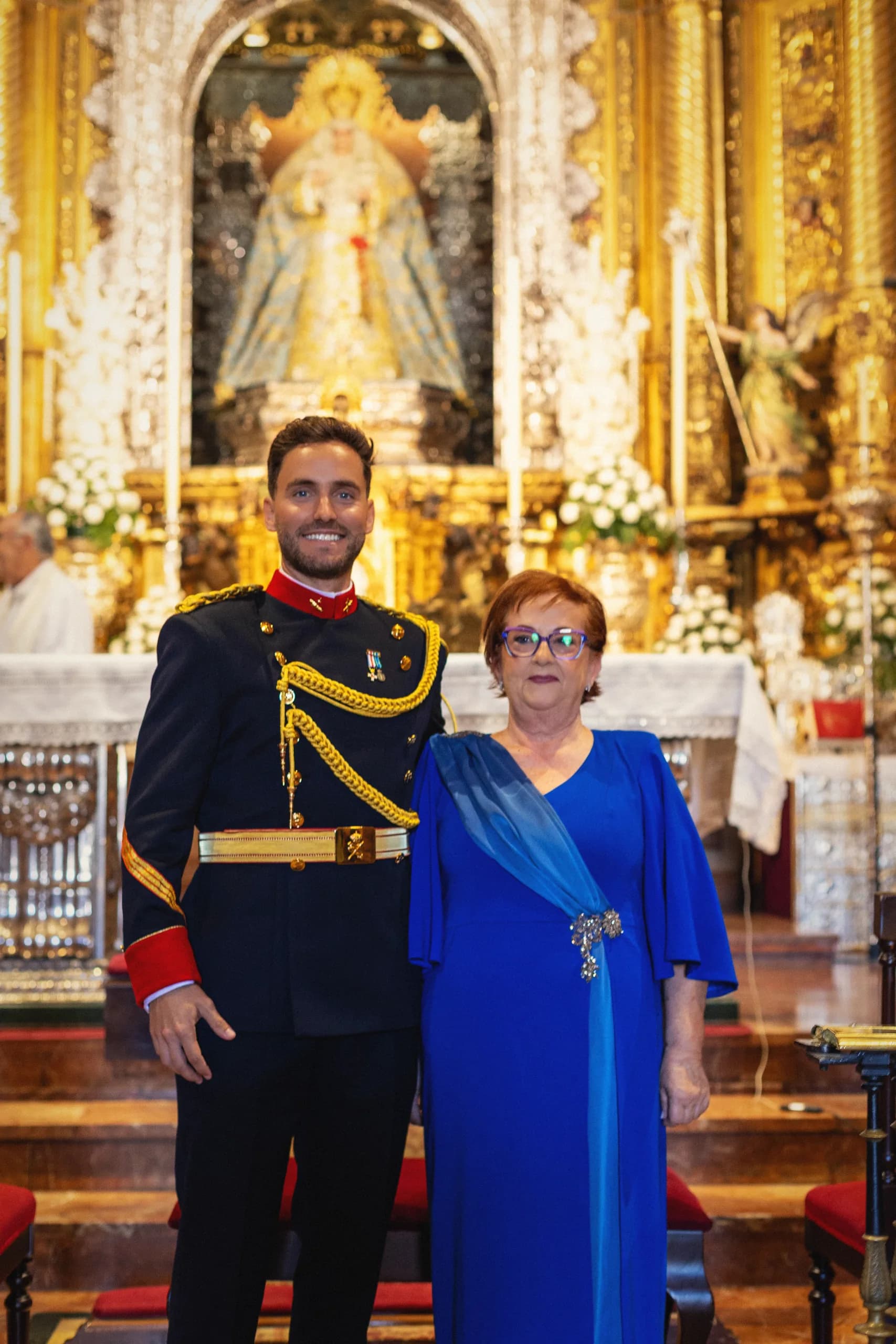 El novio de uniforme con su madre ante el retablo de la iglesia