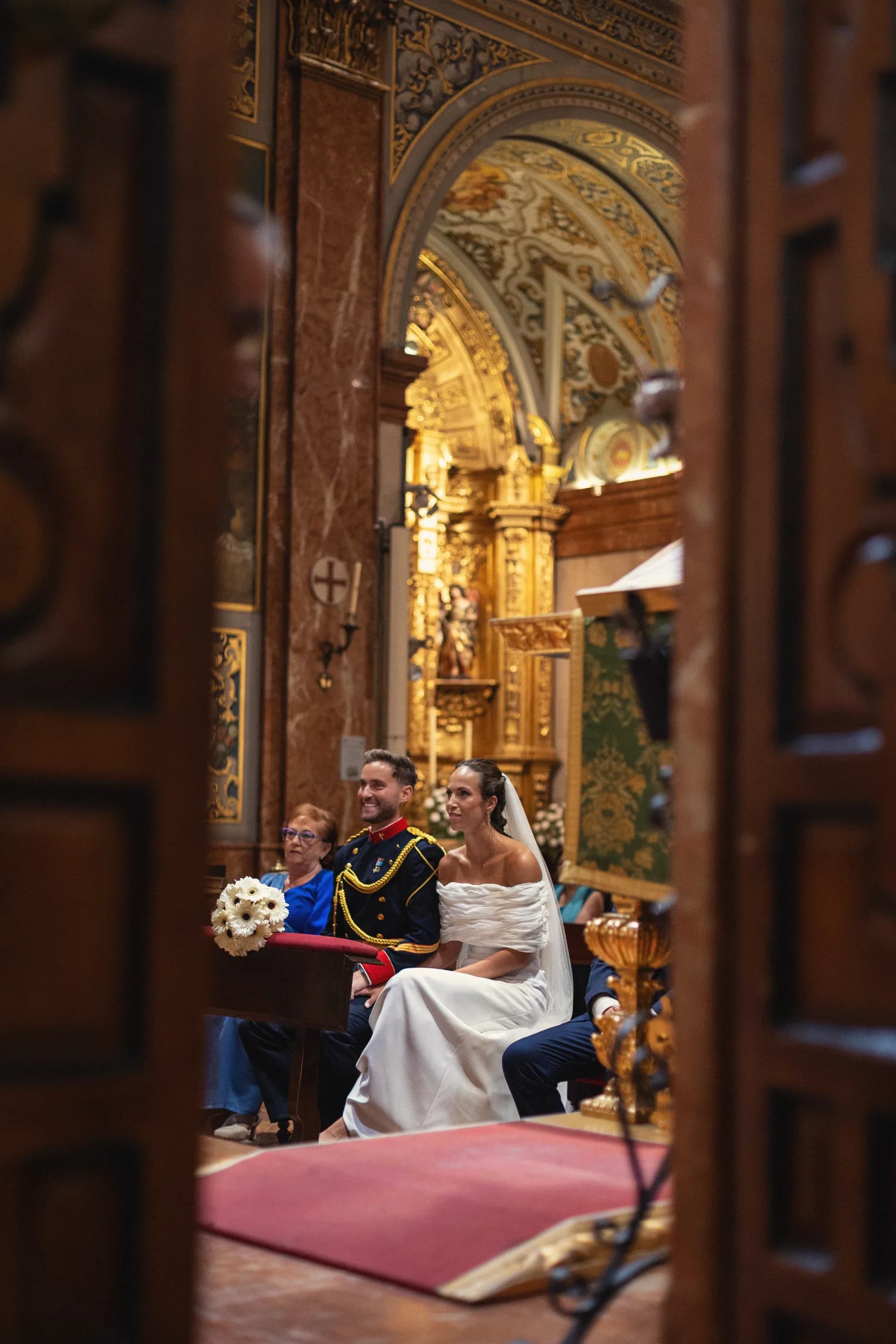 Los novios sentados durante la ceremonia, vistos desde la puerta de la iglesia