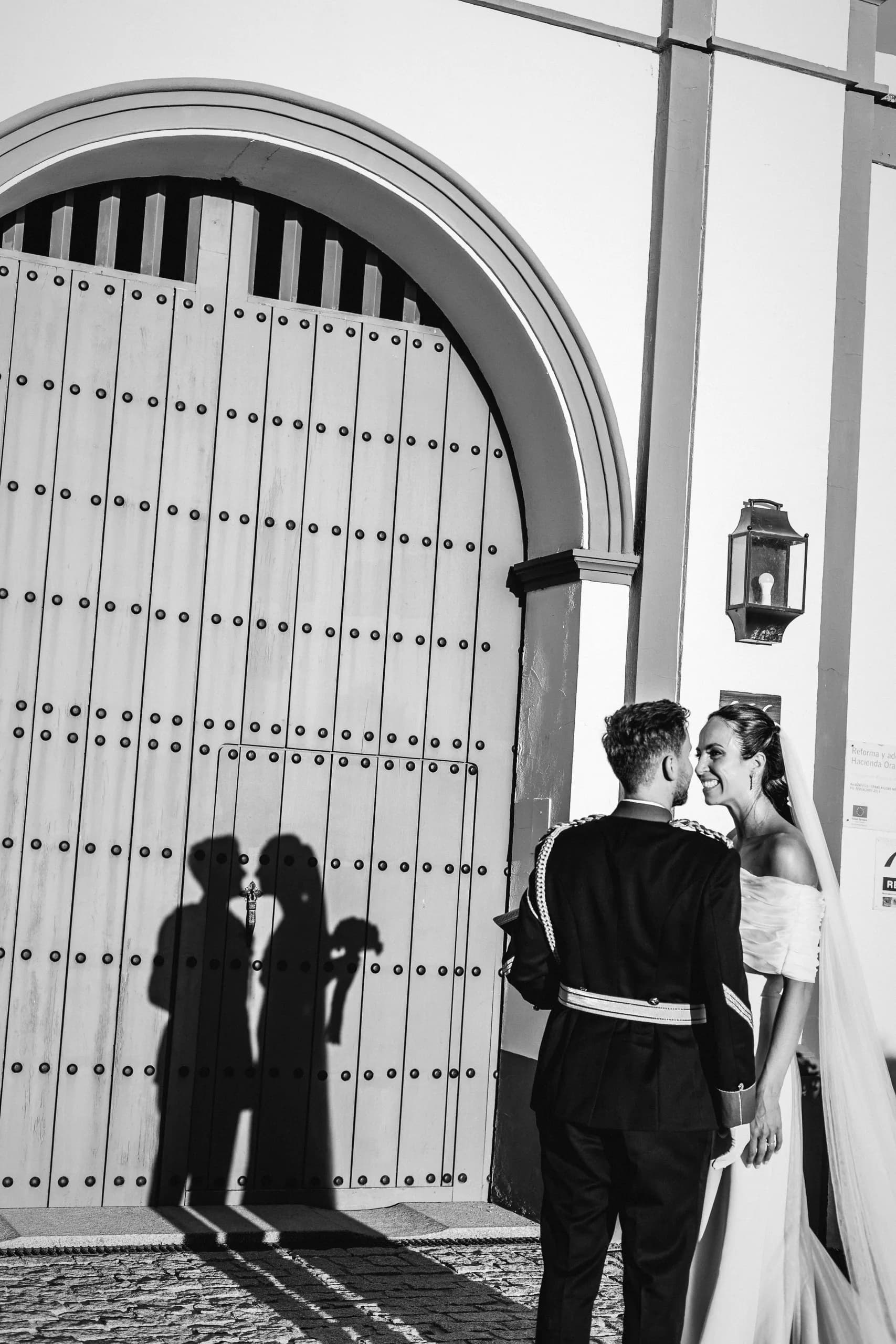 Los novios pequeñitos junto al portón de madera, en blanco y negro