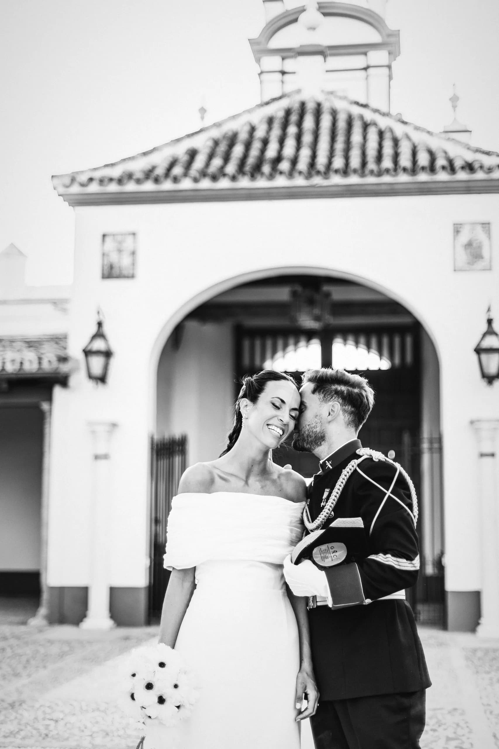 Los novios abrazados bajo el arco de la capilla, en blanco y negro
