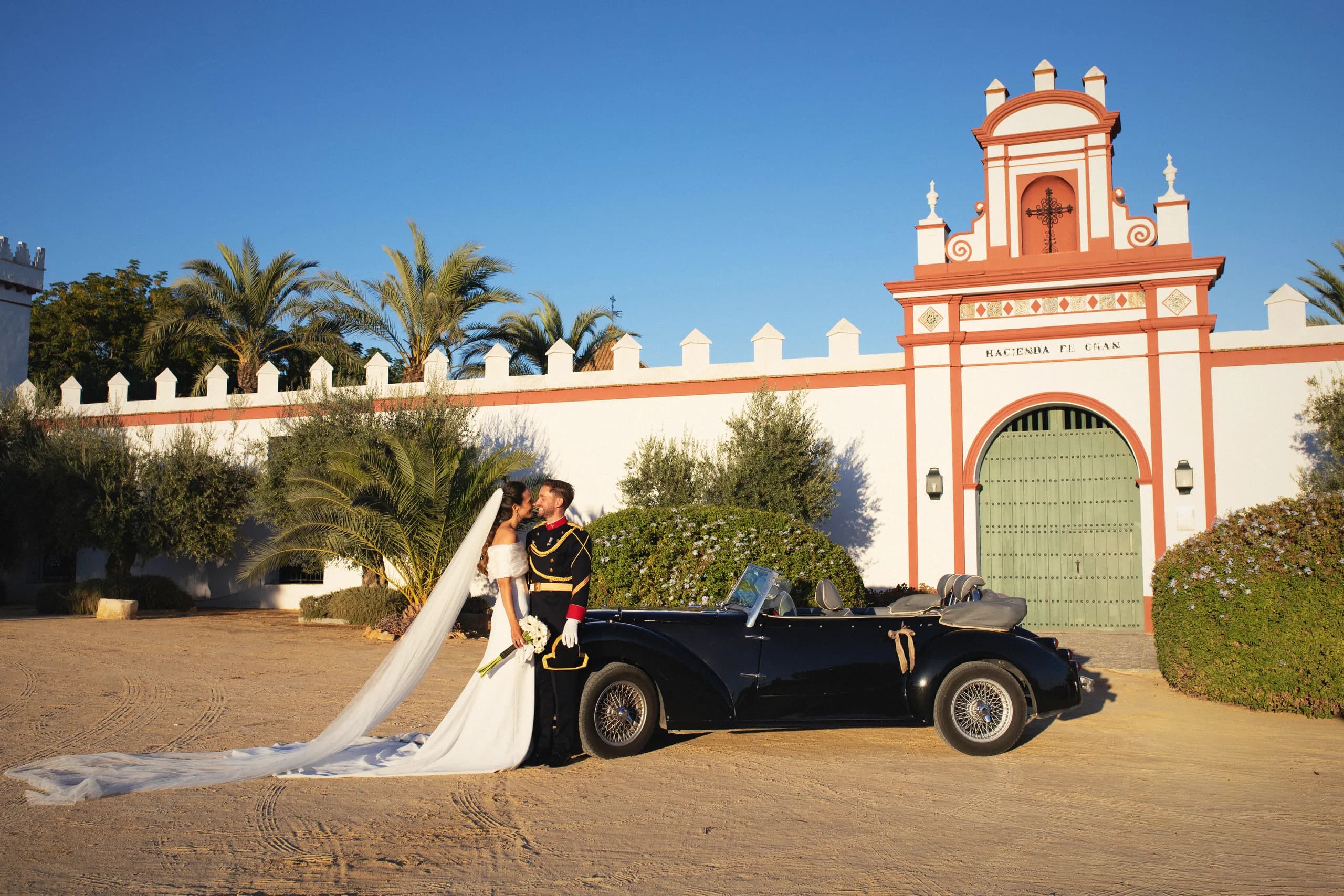 La fachada de la hacienda al atardecer, con los novios y el coche clásico delante