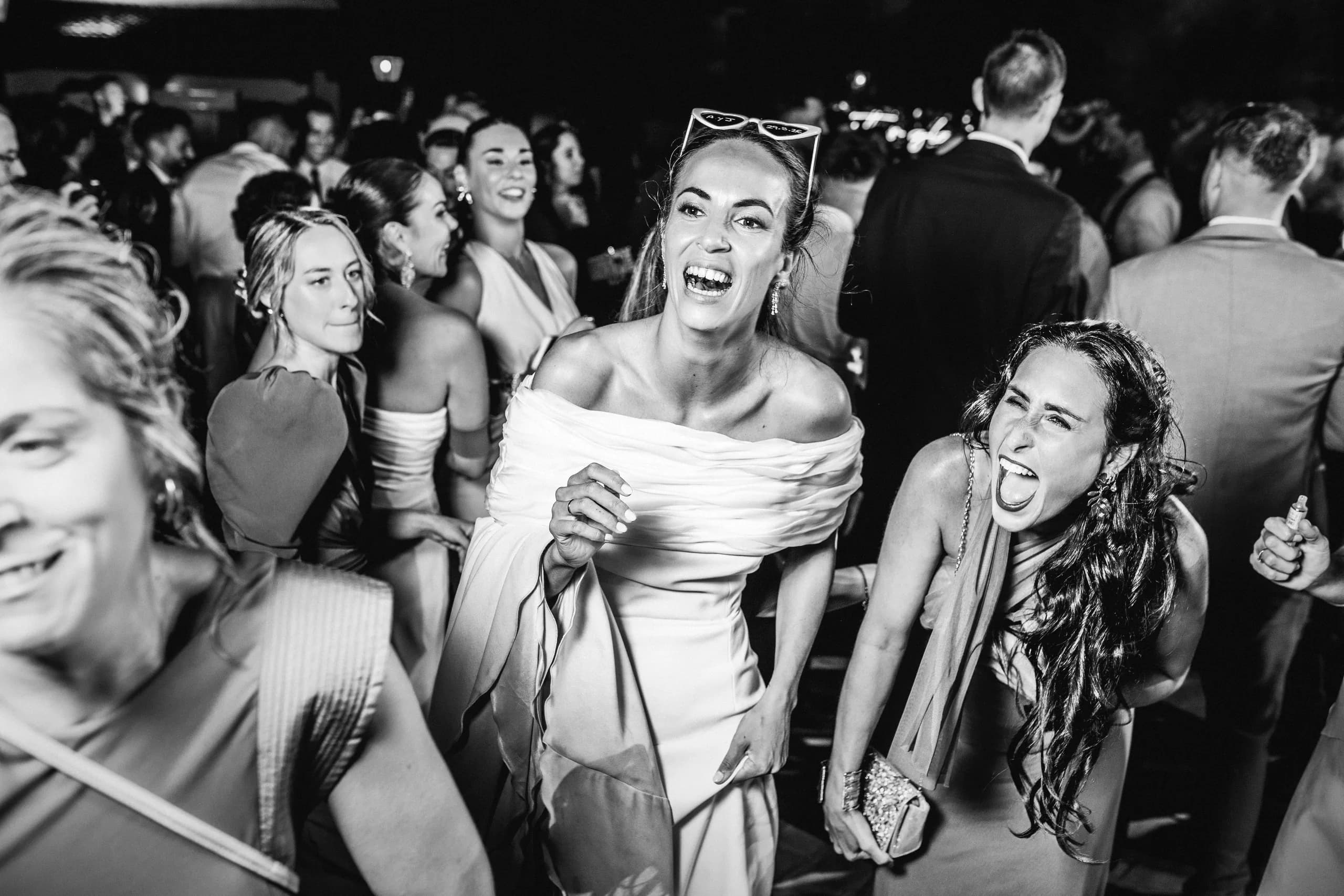 La novia riéndose entre las amigas en plena pista, en blanco y negro