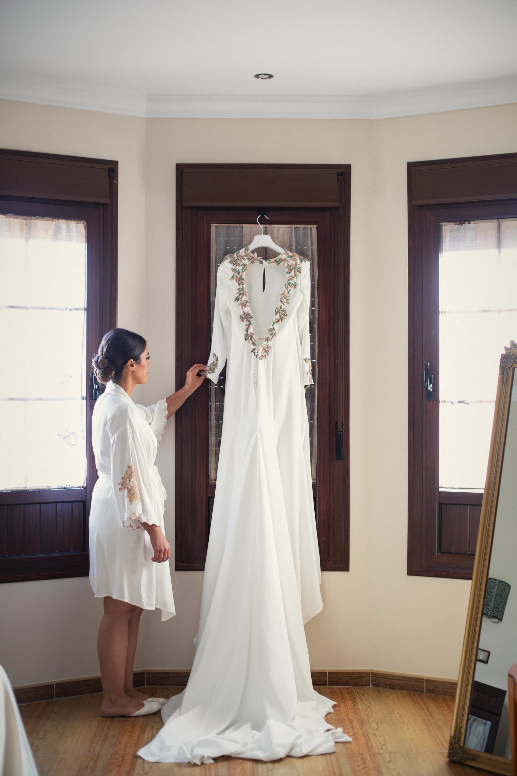 La novia mirando el vestido colgado en la ventana