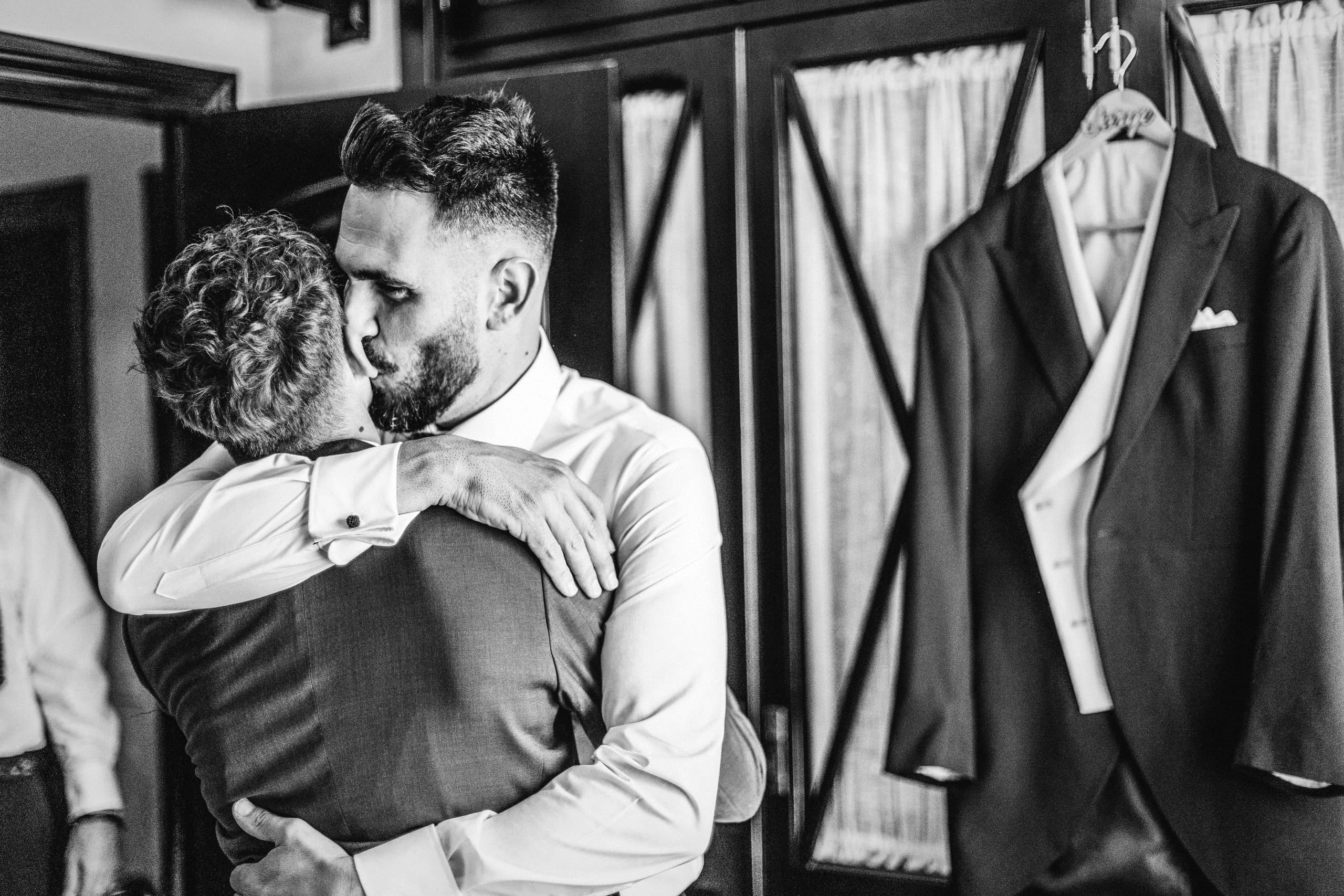 El novio abrazando a su madre junto a la chaqueta colgada, en blanco y negro