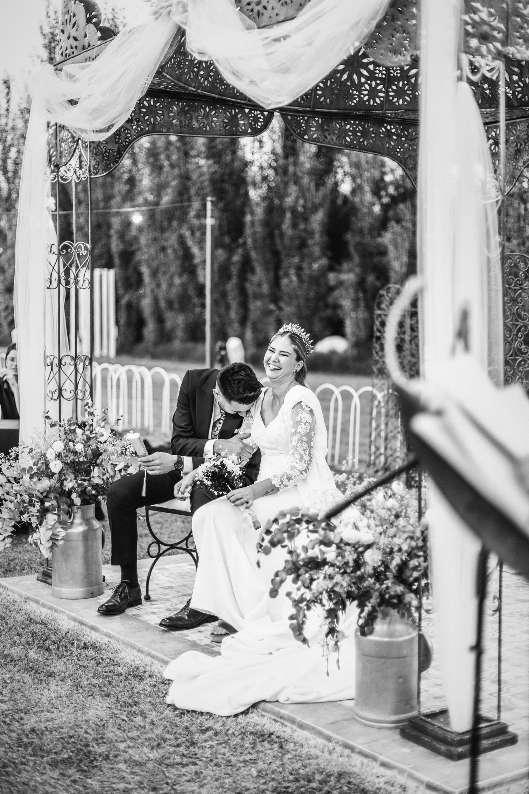 Los novios sentados bajo la carpa de la ceremonia, en blanco y negro