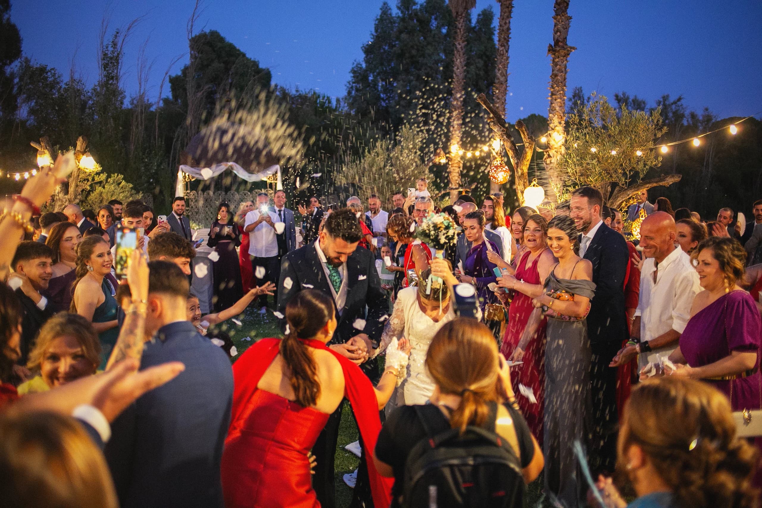 Los novios entre los invitados al atardecer, bajo las luces del jardín
