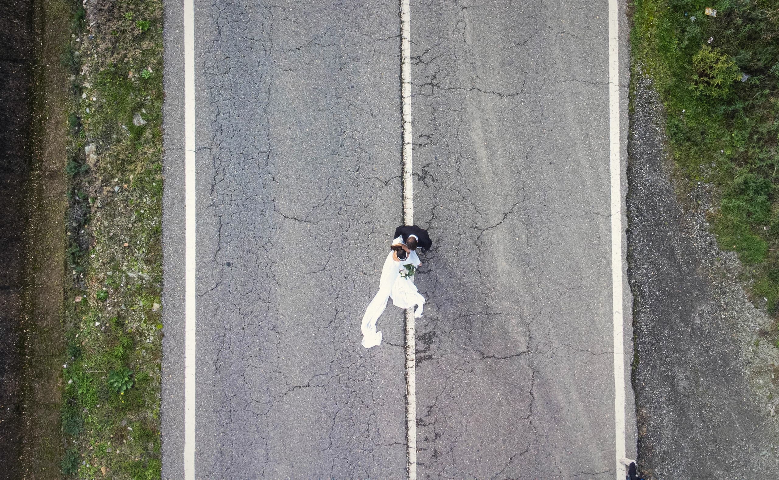 Vista cenital de los novios sobre la línea de la carretera con el velo extendido